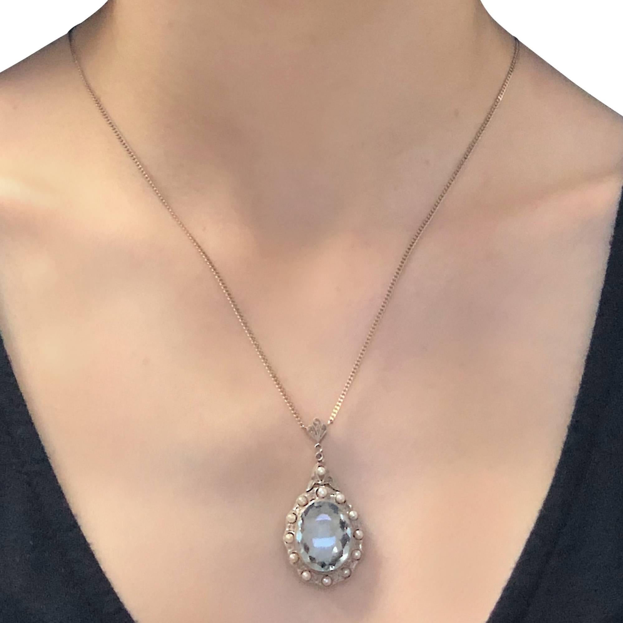 Edwardian 14k yellow and white gold pendant featuring a light blue oval shaped Aquamarine weighing approximately 7 carats, framed in millegrain, surrounded by alternating rose cut diamonds and pearls, suspended from a 14k white gold necklace. The