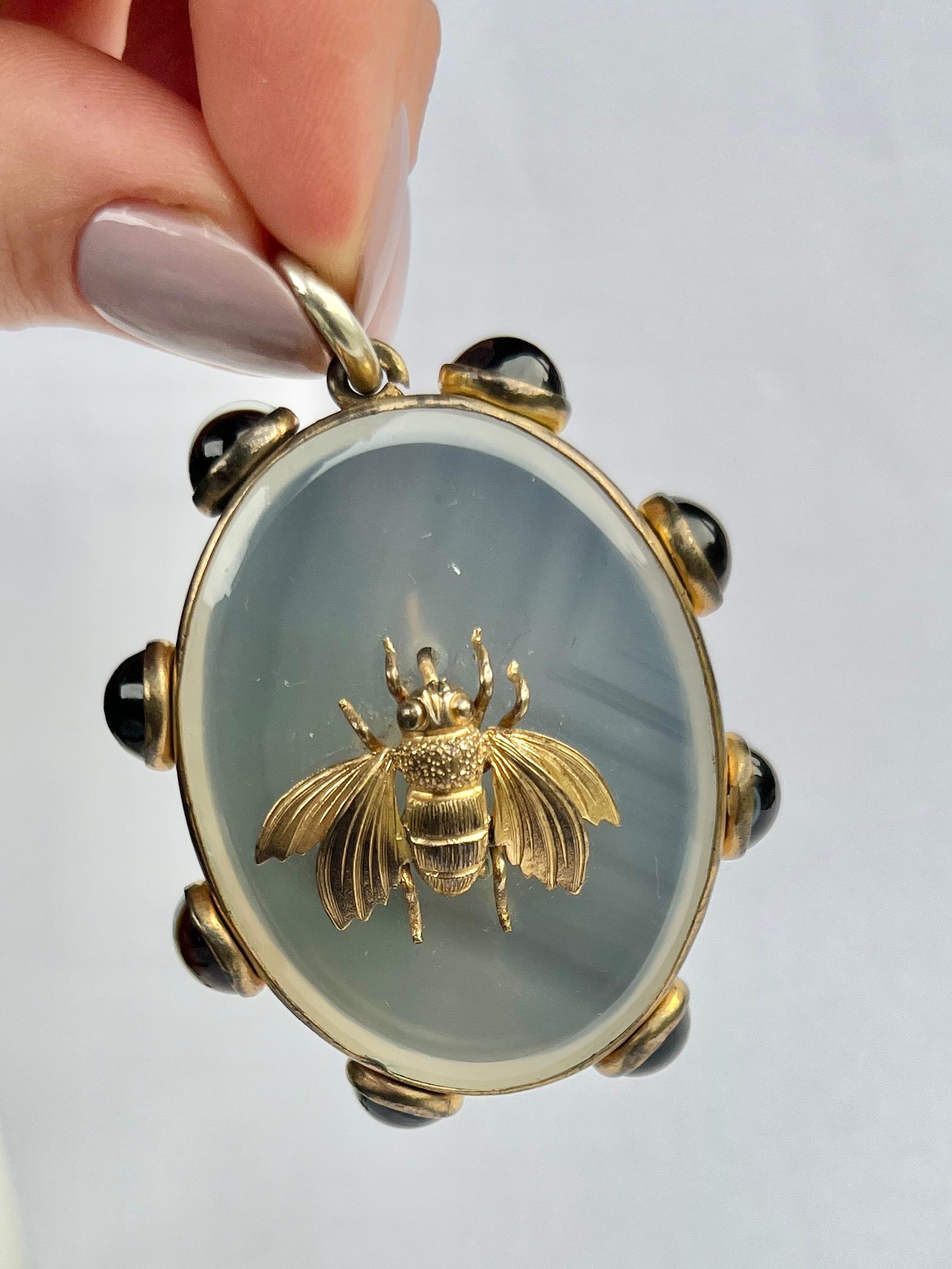 This wonderfully ornate locket has a beautifully detailed bee and holds eight glossy banded agate around the edge of the pendant. Turn over this pendant and there is a locket back with the original glazed panel. modelled in gilt. 

Locket