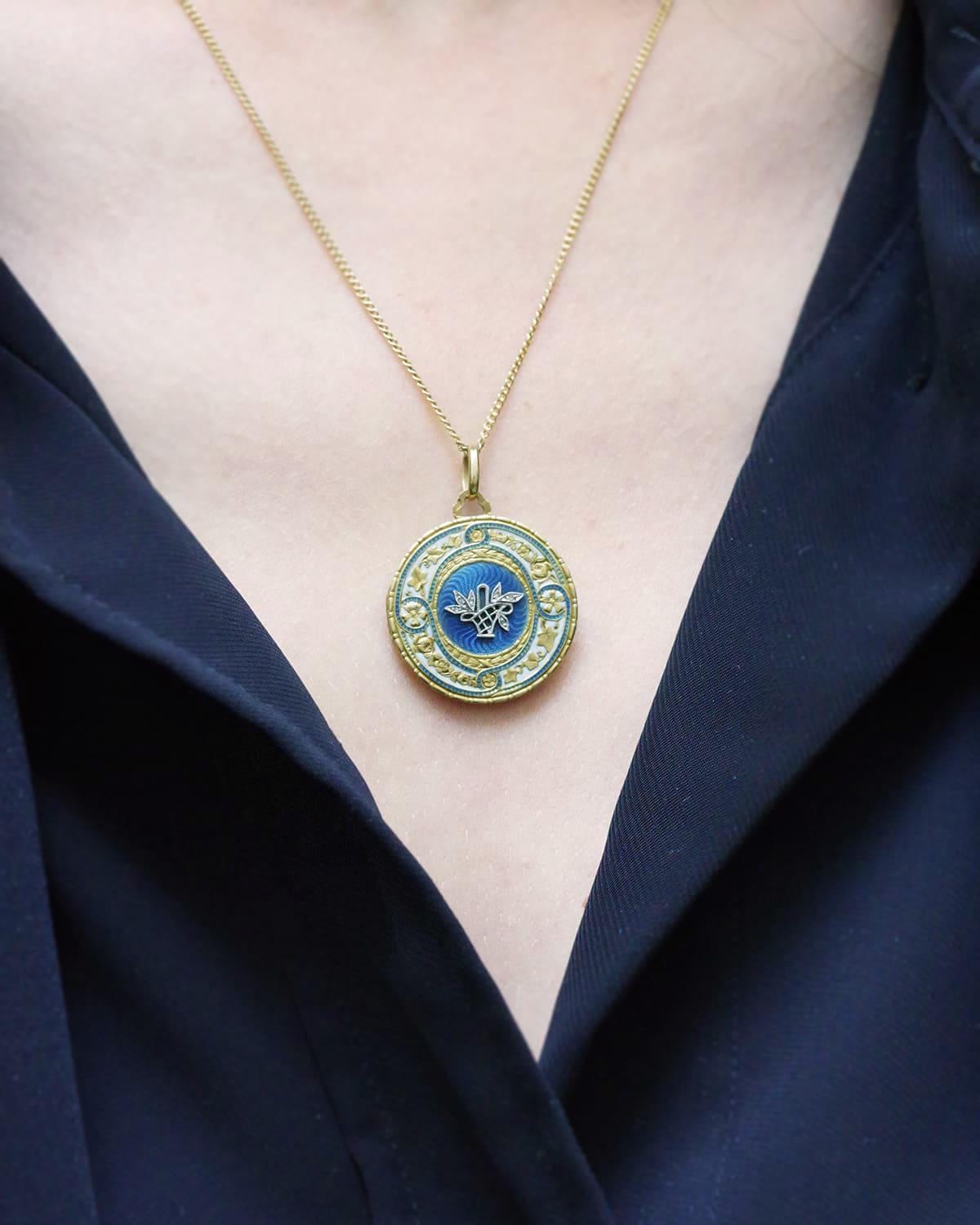 Ciondolo sentimentale edoardiano in oro 18 carati. Il medaglione rotondo con cerniera è decorato con un cesto floreale in platino con sei diamanti taglio rosa. Poggia su uno sfondo circolare di smalto blu guilloché. Questo motivo centrale è