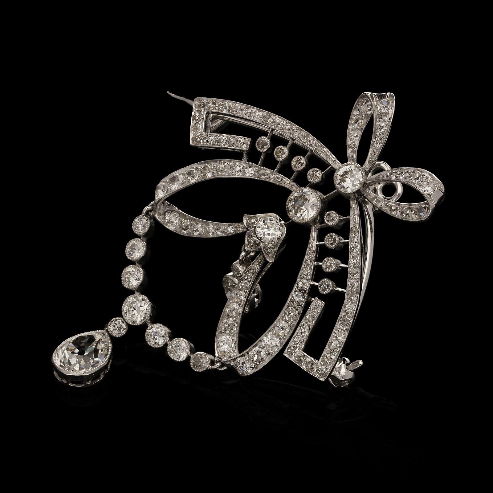 A beautiful Edwardian diamond and platinum brooch /pendant c.1910 of garland style design, the body of the pendant is circular in shape with inner swag motifs and surmounted by a stylised ribbon bow, it suspends a single pear shape old cut diamond