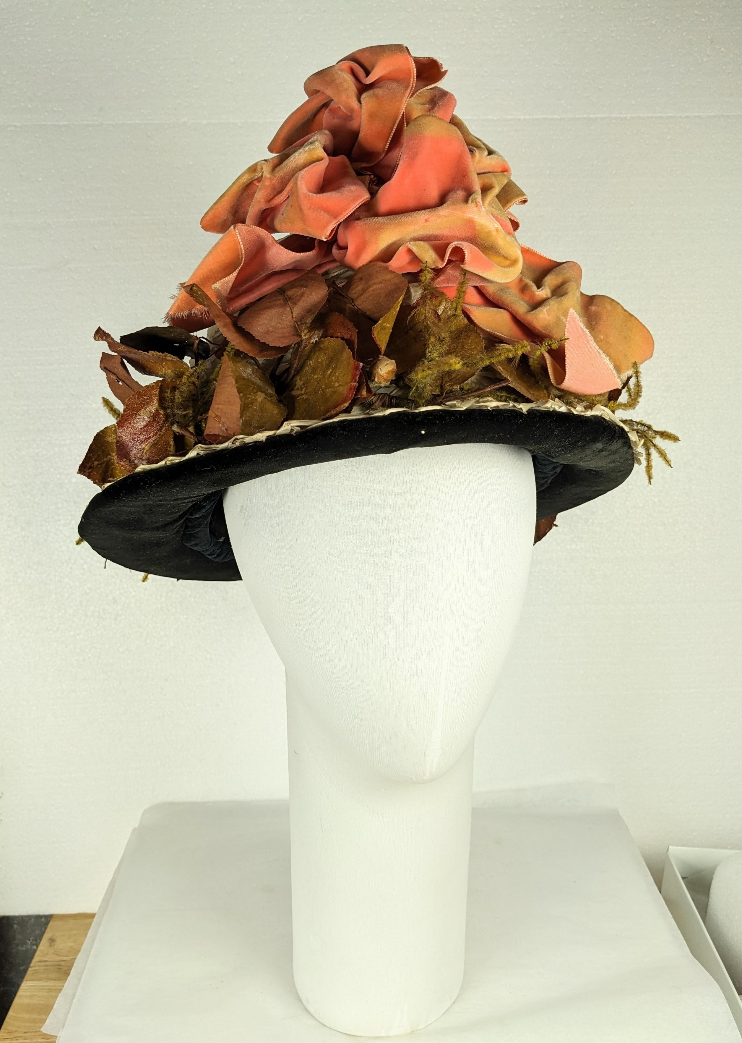 Charming Edwardian hat of natural woven raffia straw circa 1900 trimmed with massive peach silk velvet bow, naturalistic green glazed cotton leaves, and imitation moss stems. Black silk velvet brim, and black taffeta lining. Labelled: The Ideal