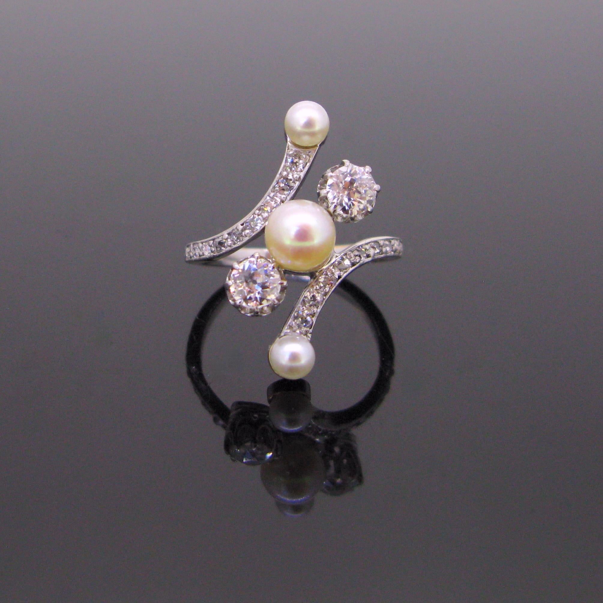  This ring is made in 18kt white gold and platinum. It has a ravishing twisted design. It is set with a natural creamy (with a touch of pink) pearl of 5,79 mm of diameter, and with 2 old mine cut diamonds each weighing approximately 0,30ct. 

The