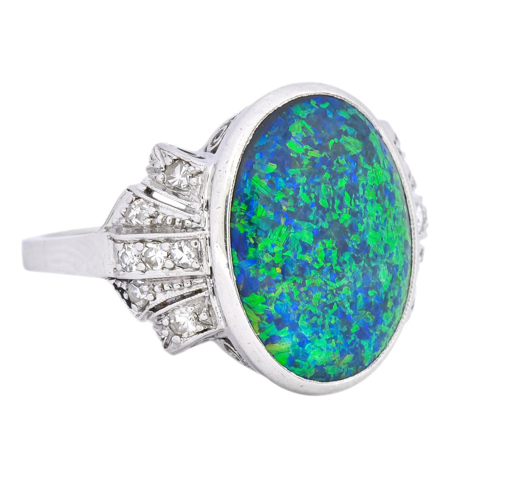 Centering a bezel set oval cabochon black opal measuring approximately 15 x 11.5 mm, with strong play-of-color including flashes of green and blue

Flanked by scrolled bow motif bead set with single cut diamonds weighing approximately 0.22 carat