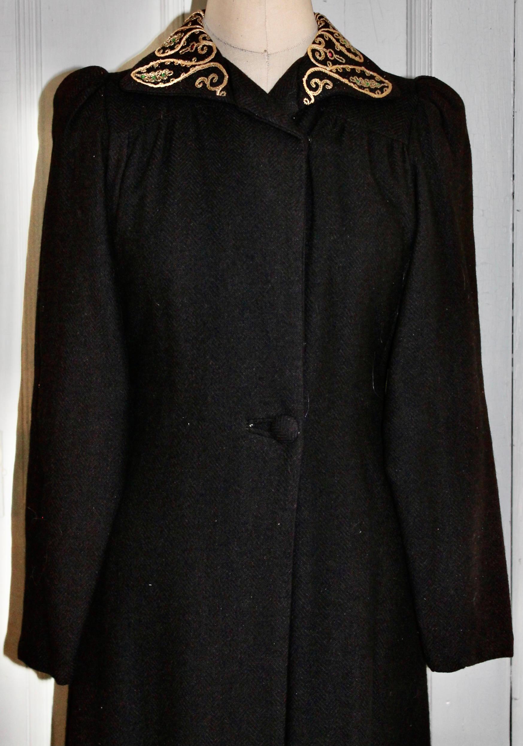 A long black Edwardian coat with a gold embroidered Indian motif collar, with faux red and green 'stones'. Slim fitted and long sleeves. Slightly padded shoulders.