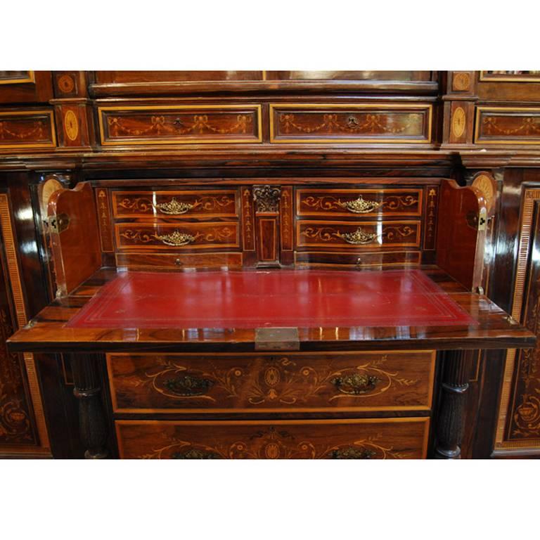 The best Edwardian period bookcase and secretaire made of rosewood with other exotic wood neoclassical architectural and floral motif inlays. The central drawer open to reveal a red leather writing pad with several drawers and hidden compartments.