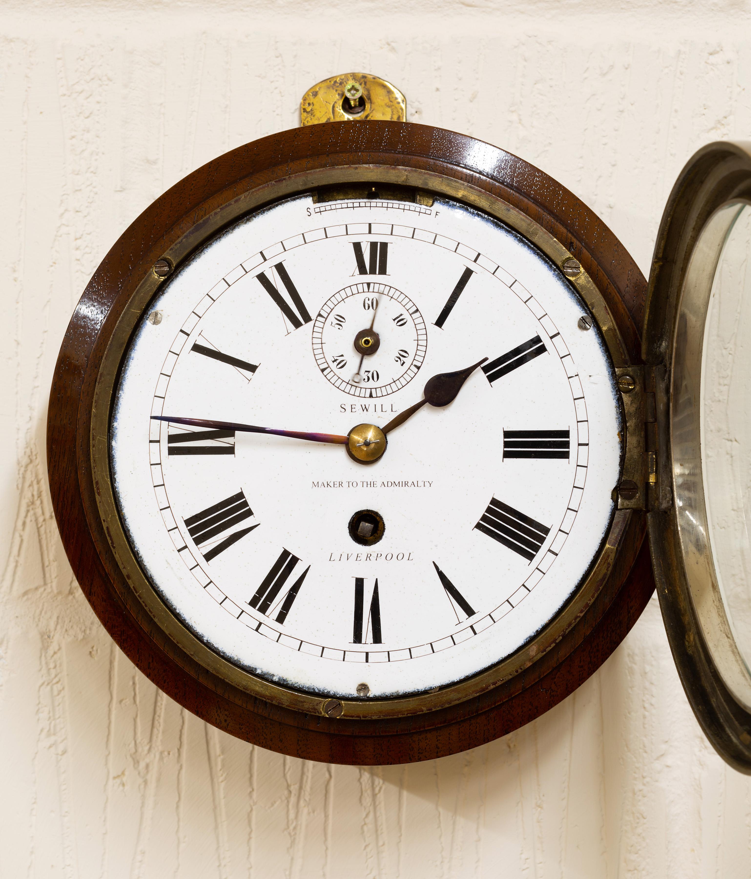 Brass ships clock with a mahogany surround, enamel dial with Roman numerals, original ‘blued’ steel hands with subsidiary dial below the XII for seconds and signed ‘Sewill, maker to the admiralty, Liverpool’.


Eight day chain Fusee movement with