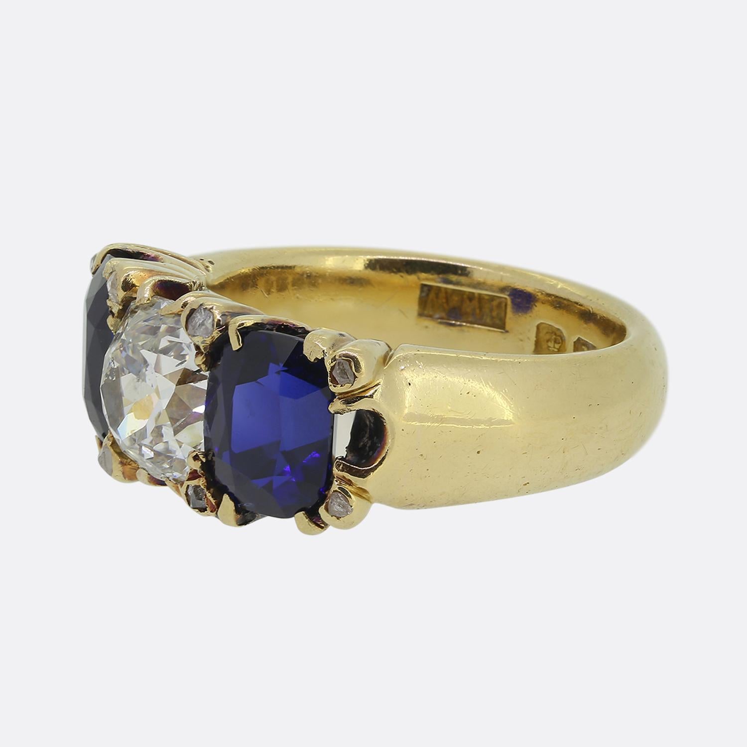 Aquí tenemos un llamativo anillo de tres piedras de la época eduardiana. Esta magnífica pieza se ha elaborado en oro amarillo de 18 ct y lleva un impresionante diamante cuadrado antiguo de talla cojín en el centro de la cara. Flanquean a esta piedra