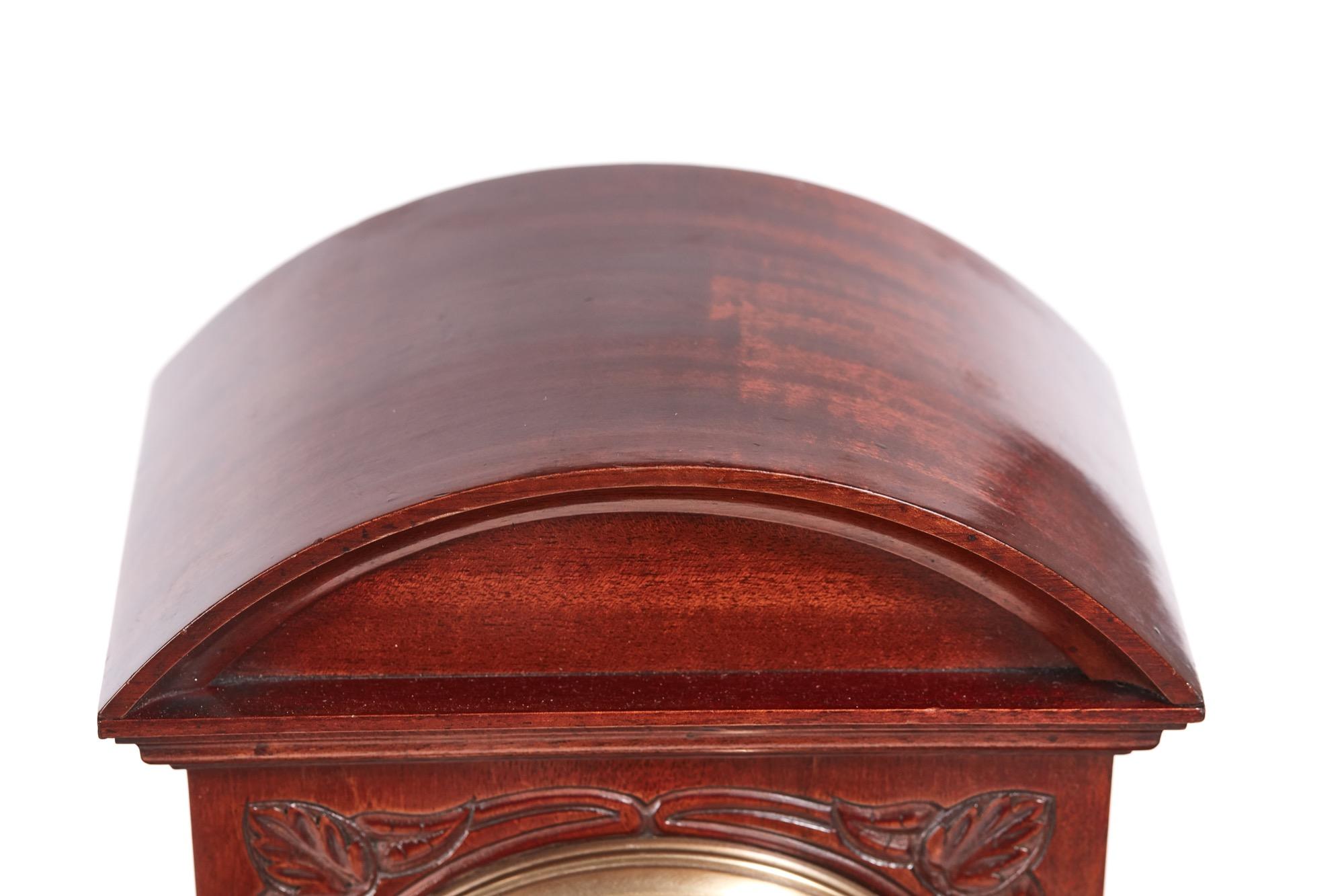 Edwardian carved mahogany mantel clock having an arch top and well carved mahogany case with a stepped base standing on brass ball feet. The enamel dial has a brass bezel and convex bevel edge glass, eight-day movement striking the hour and halves
