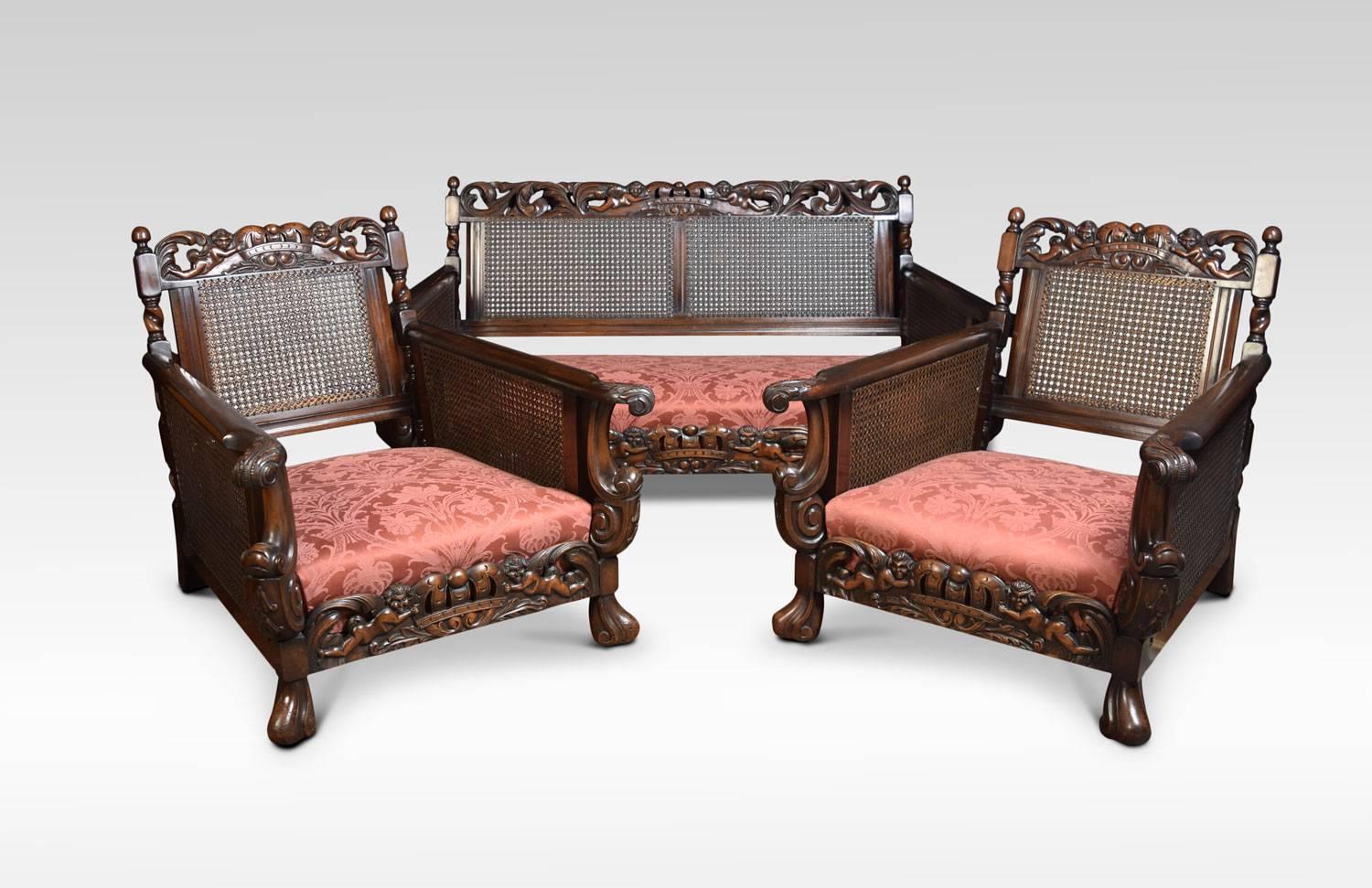 Mahogany framed lounge suite comprising of three-seat settee and pair of armchairs, all having carved back rail with cherub decoration. The bergere panelled back and double skin sides, enclosed by out swept scroll and foliate carved arms, raised on