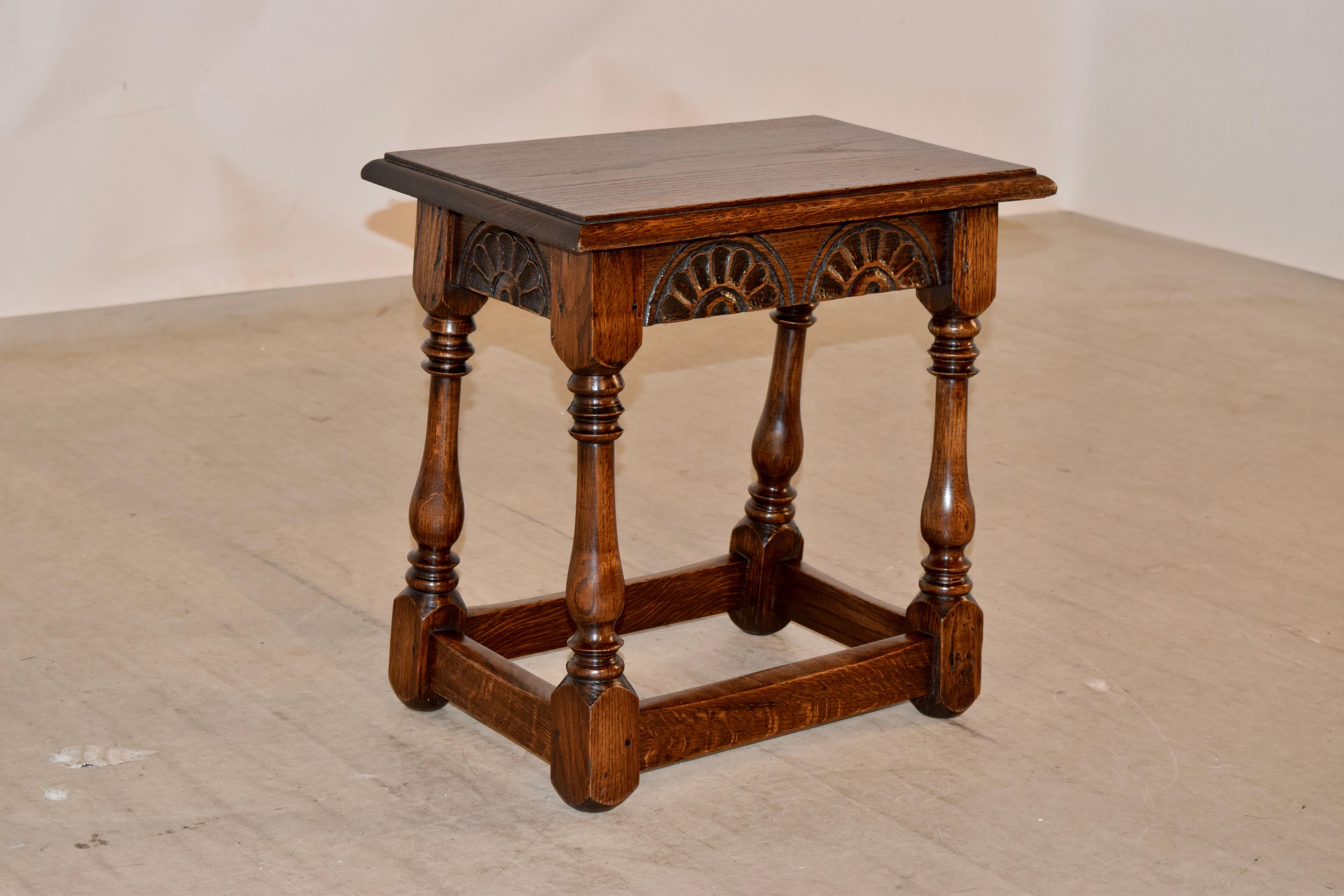 English oak joint stool with a beveled edge around the top following down to hand carved decoration on all four sides of the apron, circa 1900. The stool is supported on hand turned and splayed legs, which are joined by simple stretchers.
