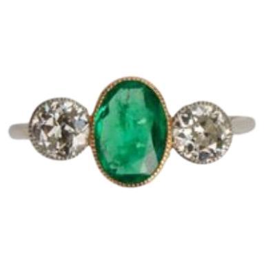 An early-twentieth century trilogy ring (designed with three stones to represent the past, present and future). This wonderful ring centres on an oval Columbian emerald in a yellow gold millegrain collet, set between white gold millegrain collet-set
