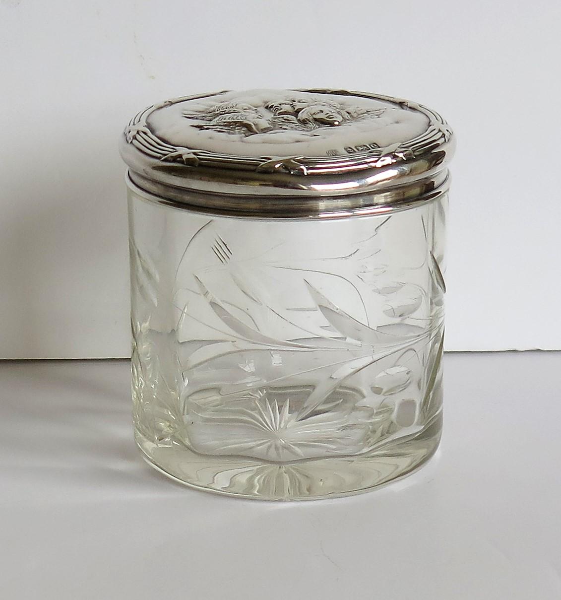 This is a very attractive English Edwardian period crystal cut glass engraved bottle or small Jar with a sterling silver lid, hand decorated in an Art Nouveau winged cherub design and marked Birmingham, 1904.

The bottle or jar is crystal cut