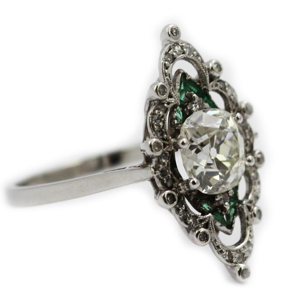 A vibrant Edwardian diamond and emerald ring, set in platinum. Centering old cushion cut diamond and small emerald and surrounded by scrolls of diamonds. This ring is a fine example of Edwardian elegance and the jewellers art, the details design and