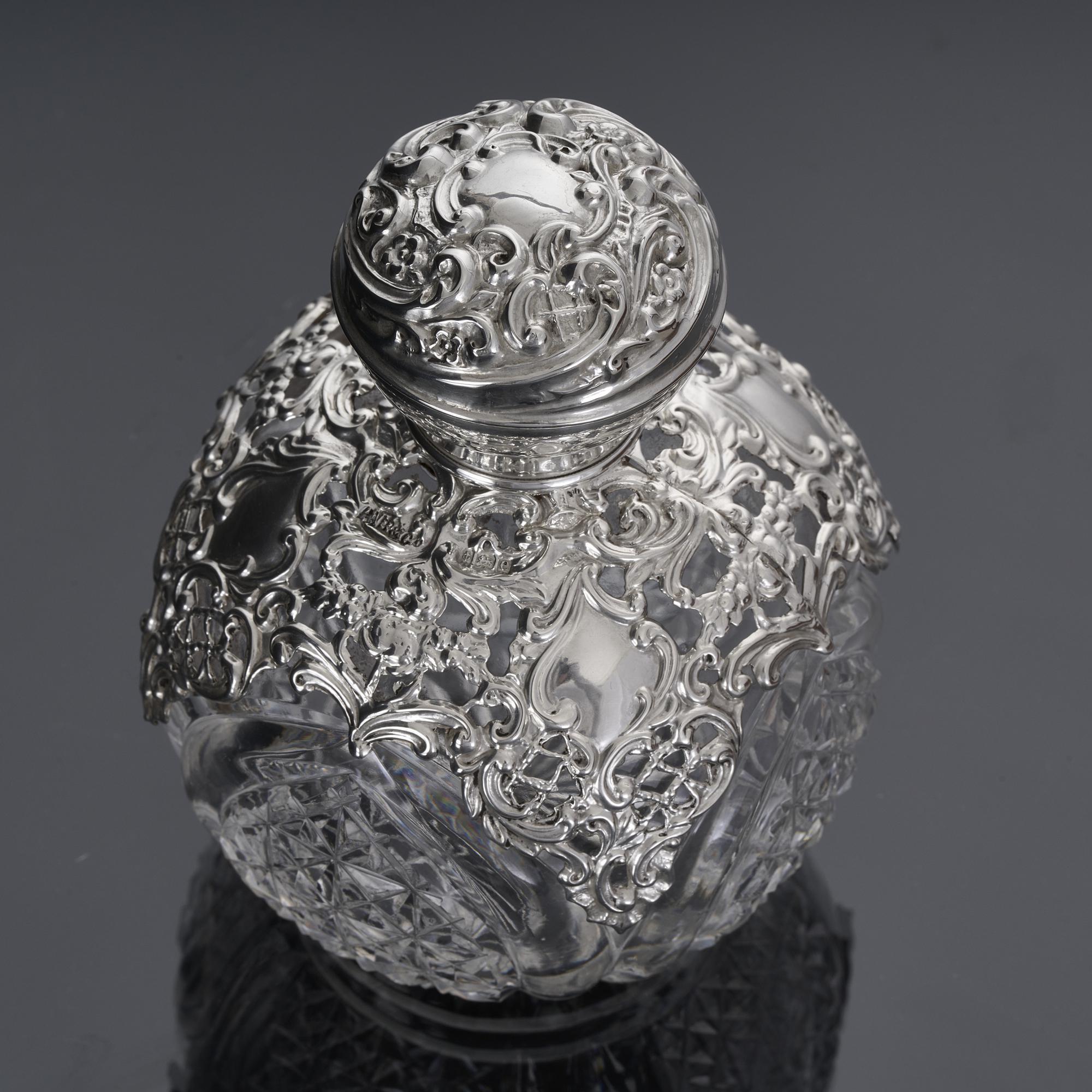 Antique cut glass globe perfume bottle from the Edwardian era.  The round body is decorated with sections of hand cut diamond starburst patterns, and fitted with an open-work sterling silver apron and hand embossed silver pull-off cover. The