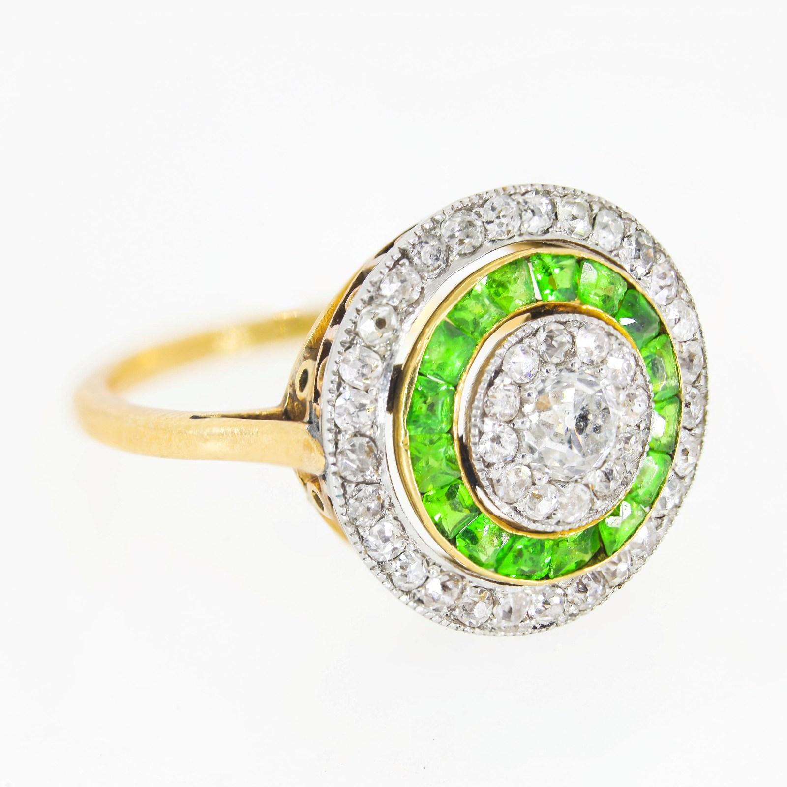 Created by hand of platinum topped 18KT yellow gold, this 1910-1920  Edwardian ring is one-of-a-kind stunner.  The Old Mine cut diamond at the center weighs 0.35 carat, surrounded by concentric rings of calibre bright Demantoid Garnerts and forty