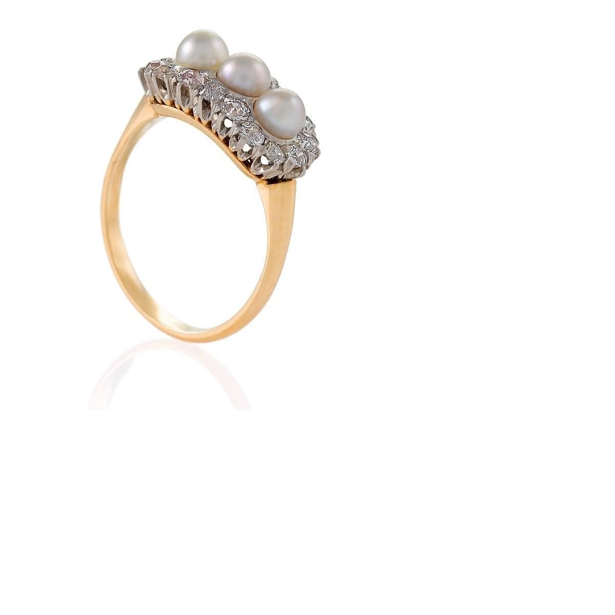 Dieser romantische Ring ist perfekt edwardianisch mit seinen drei cremefarbenen, schimmernden Perlen, die in Platin gefasst sind, inmitten eines Nestes von brillant funkelnden Diamanten. Das Gleichgewicht zwischen den milchigen Perlen und den