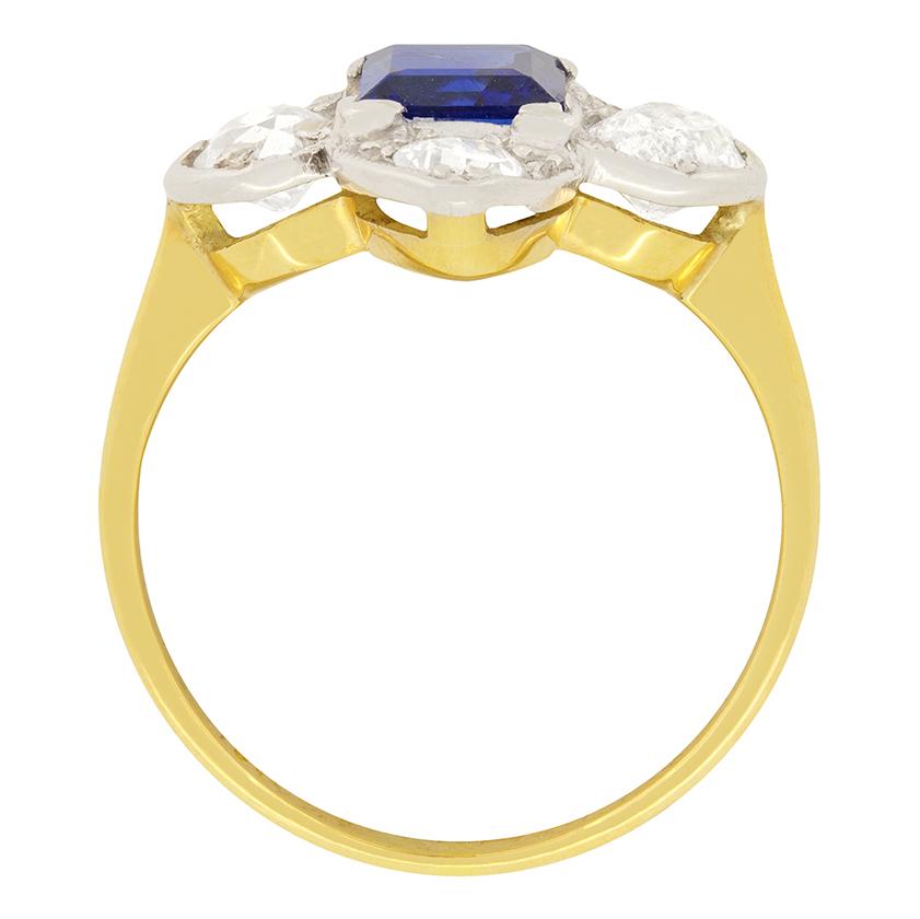 This fashionable Edwardian two-tone diamond and sapphire cluster ring dates around 1910. It has a beautifully coloured sapphire, weighing 0.65 carat, and is embellished by one old cut diamond at each of the cardinal points. These shining diamonds