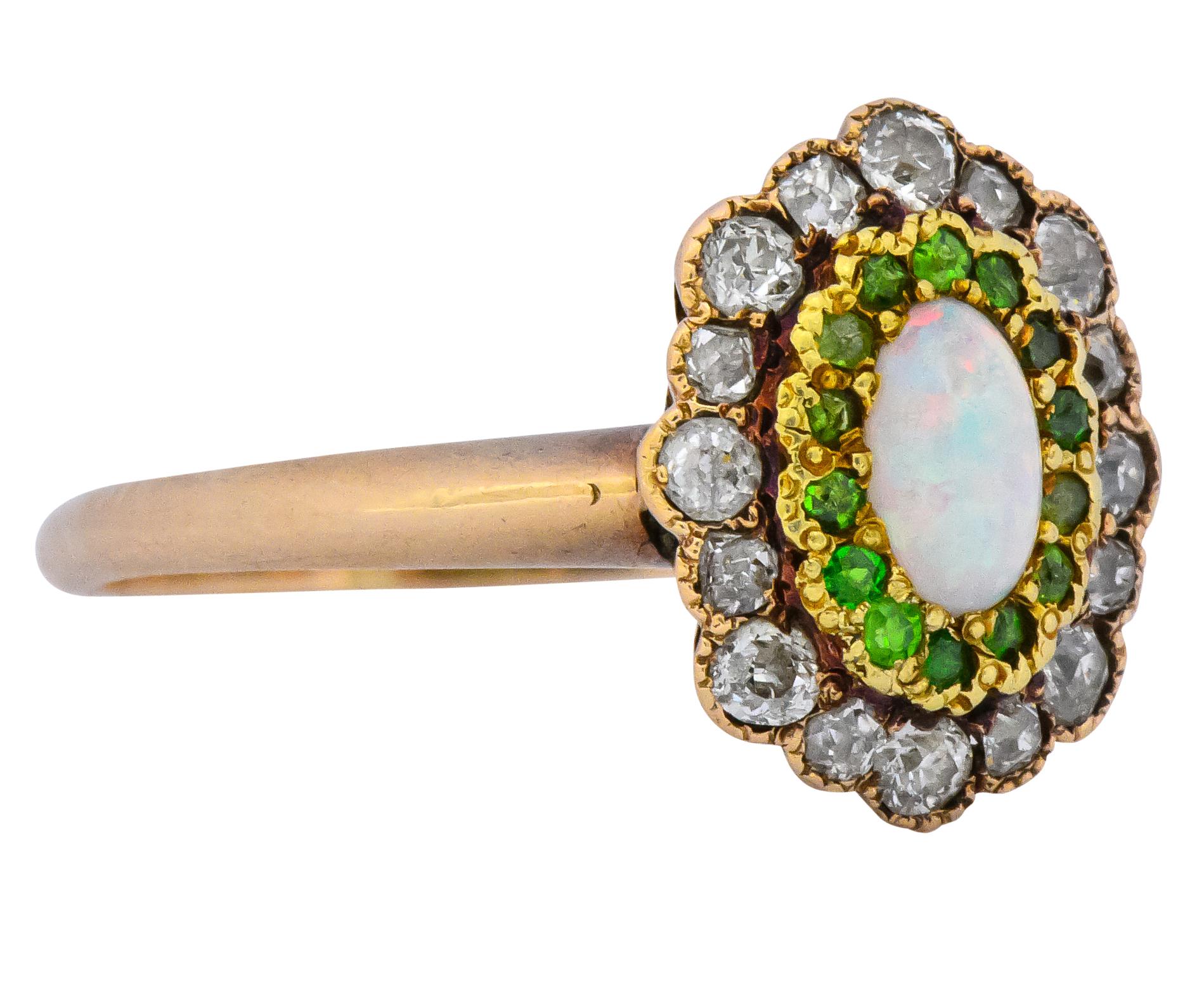 Cluster style ring centering a cabochon cut white opal measuring approximately 6.0 x 4.0 mm

Translucent and excellent play-of-color with flashes of red, yellow, green, and blue

Accented by Swiss cut demantoid garnets set in bright yellow 14 karat