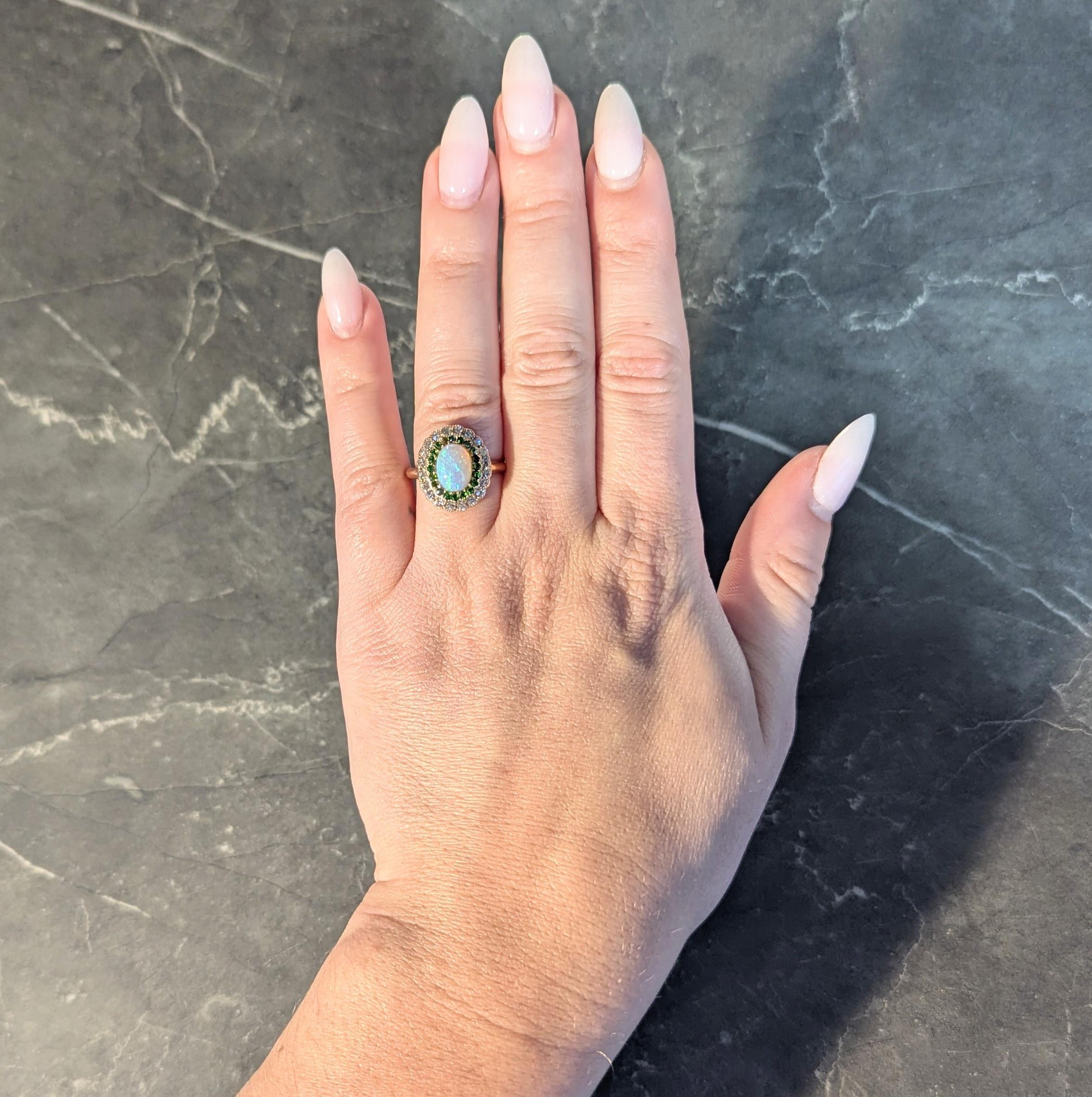 Centering an oval shaped opal cabochon measuring 6.0 x 8.5 mm
Translucent white in body color with spectral play-of-color
Bead set with a halo of round cut demantoid garnets
Weighing approximately 0.40 carat total - vibrant green in color
Bead set