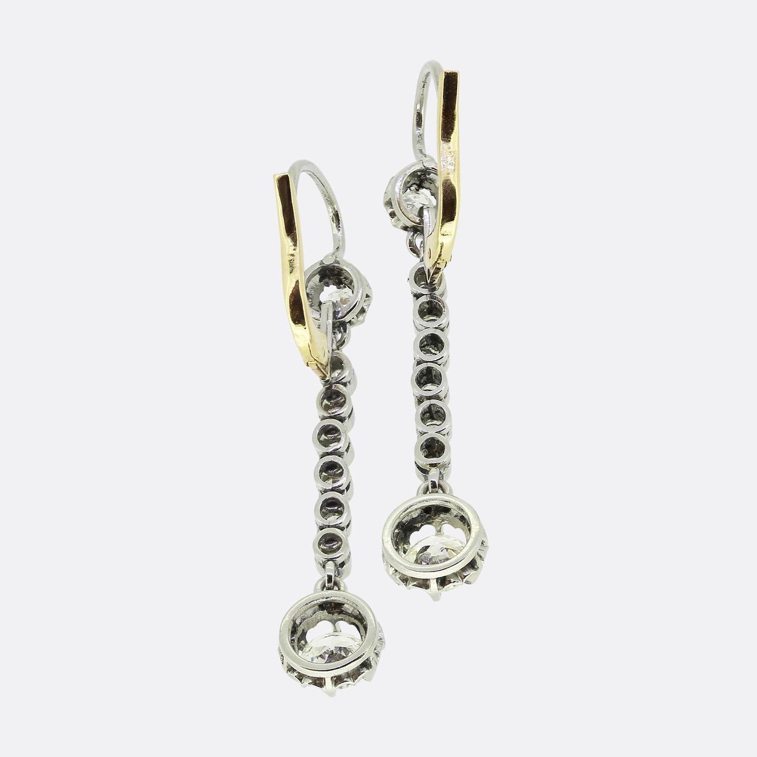 Here we have an elegant pair of diamond drop earrings dating back to the Edwardian period. Both pieces showcase a single round faceted old European cut diamond at the top which sits in a buttercup setting and plays host to a single row of freely