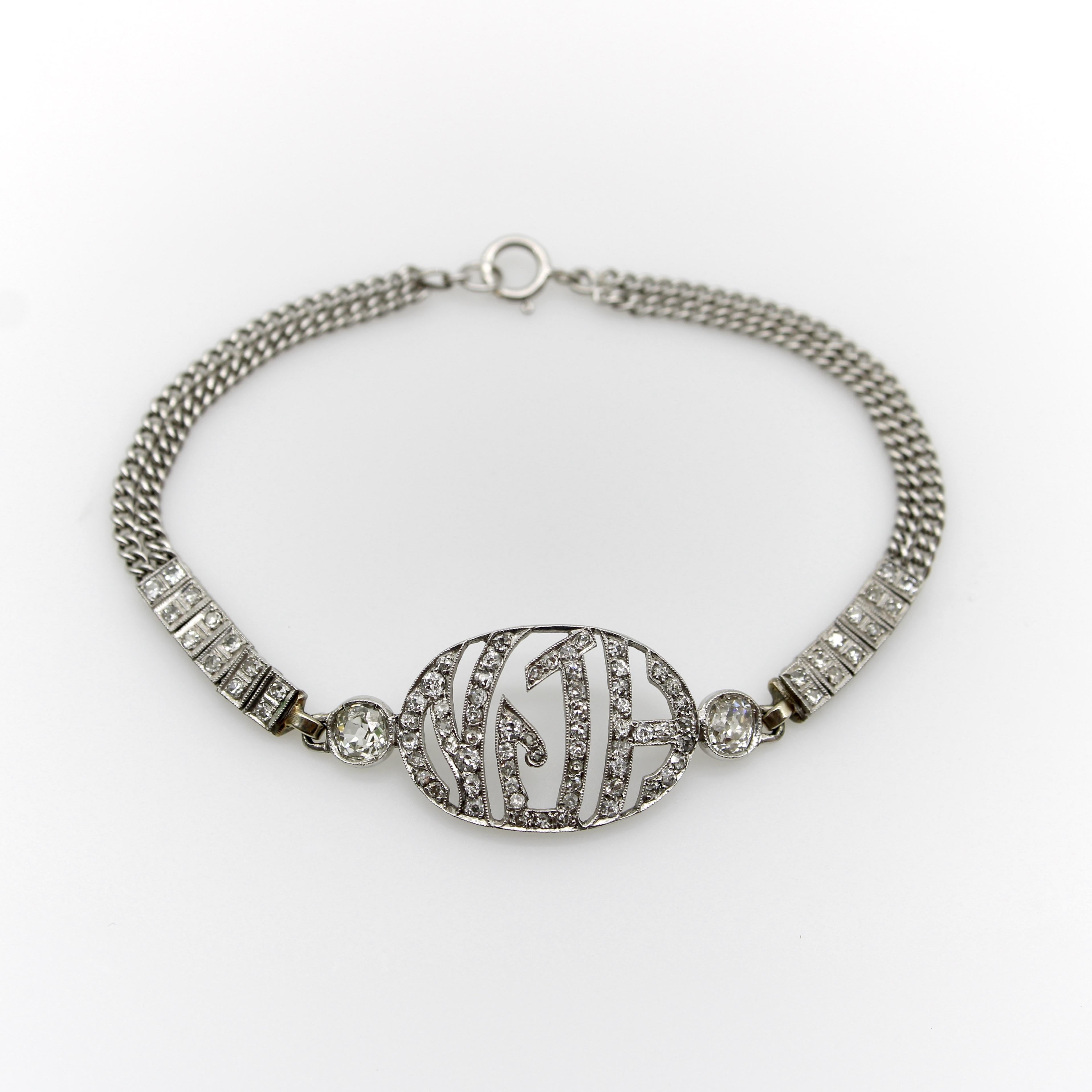 Questo bellissimo bracciale Monogram edoardiano presenta una combinazione di diamanti Old Mine Cut e diamanti antichi a taglio singolo in oro bianco 10k. Il punto focale del bracciale è un delicato ovale con le iniziali NJH in un carattere Art