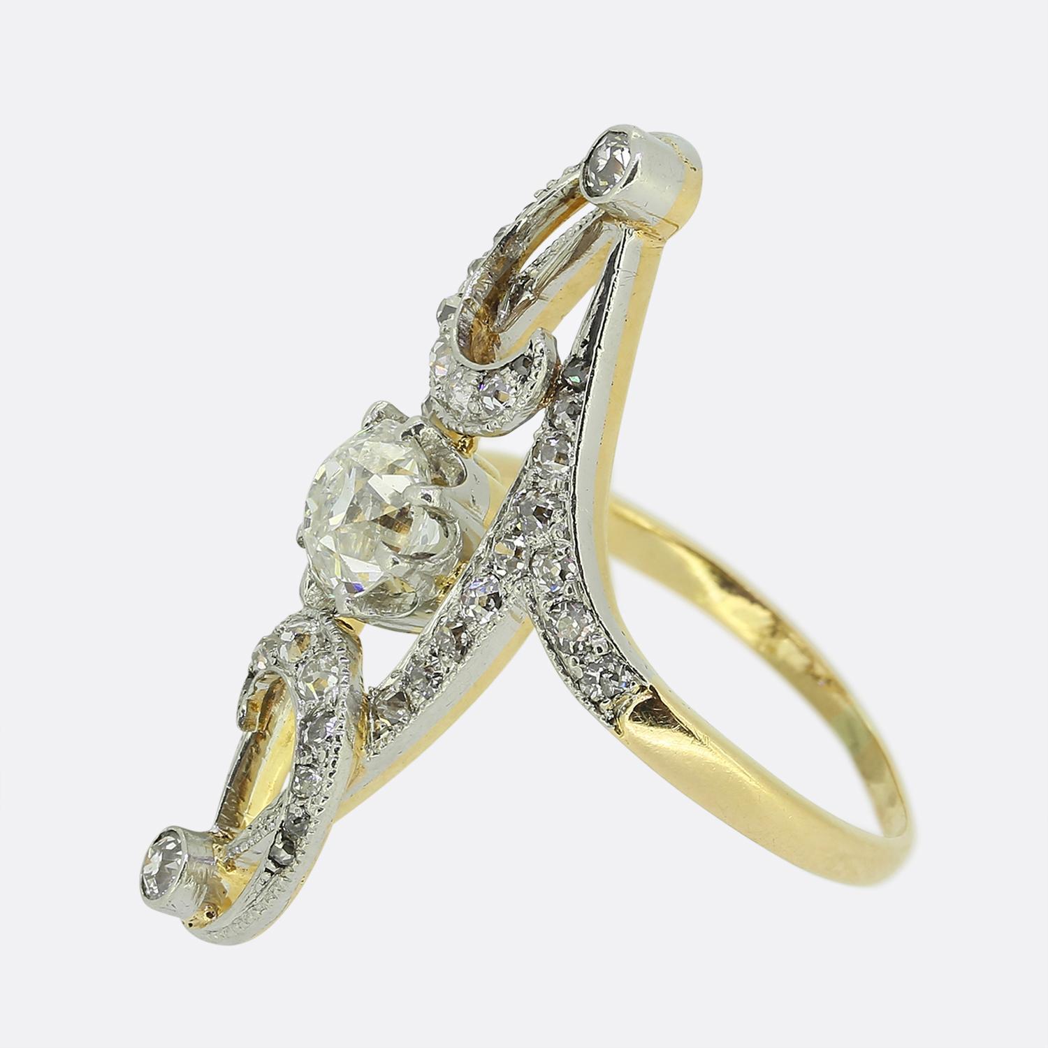 Here we have a charming navette ring dating back to the Edwardian period. This elegant piece showcases a single old mine cut diamond at the centre of the face in an eight clawed setting. This principal stone is surrounded by a curvaceous open frame
