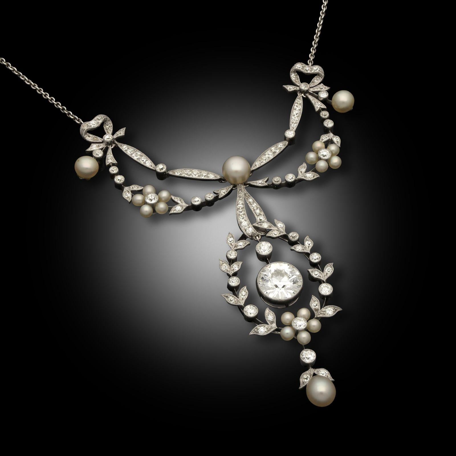 An Edwardian pearl & diamond garland necklace by the Goldsmiths & Silversmiths Company, circa 1910. The diamond and platinum pendant necklace designed as delicate ribbon, bow and garland style accented with natural pearls. The central old European