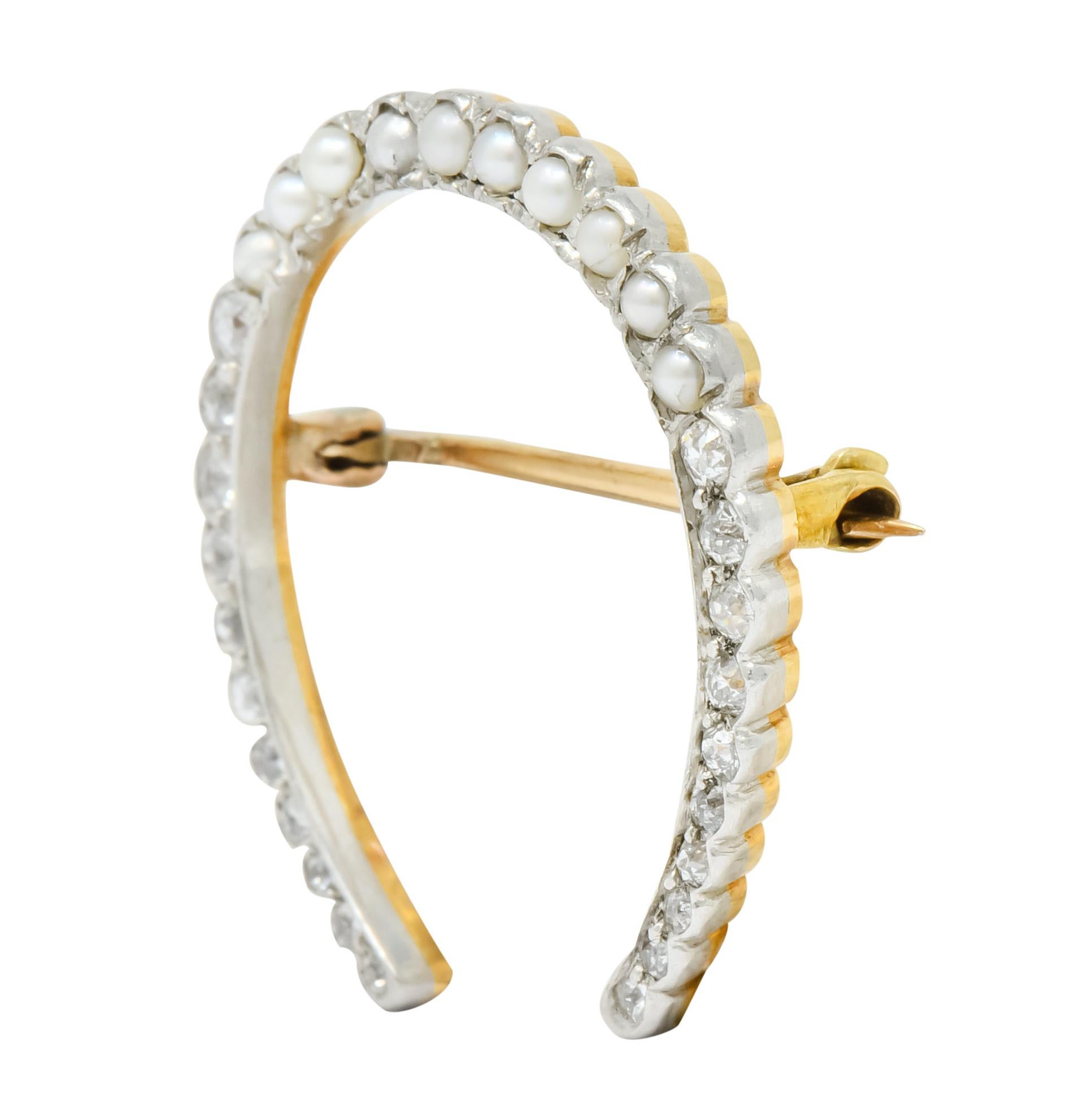 Designed as a horseshoe with a scalloped platinum edge

Set with old European cut diamonds weighing approximately 0.25 carat total, H/I color and SI clarity

Accented by round seed pearls measuring approximately 1.5 mm

Completed by gold pin stem