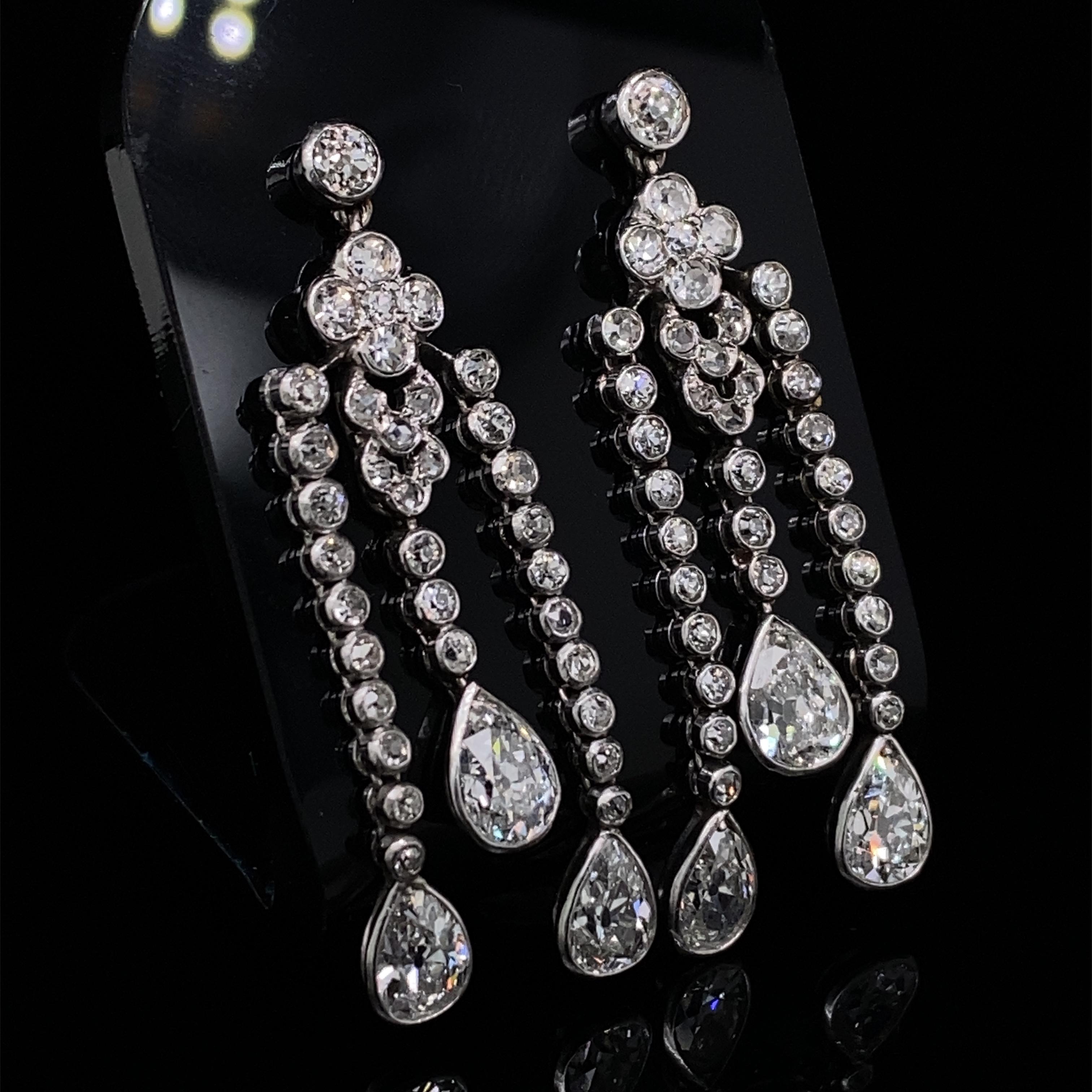 A pair of Edwardian diamond pendant drop earrings in platinum.

Each earring is designed with a floral set top, which suspend three diamond line drops all terminating in an elegant, individual rubover Old European pear-cut diamond.

All the stones