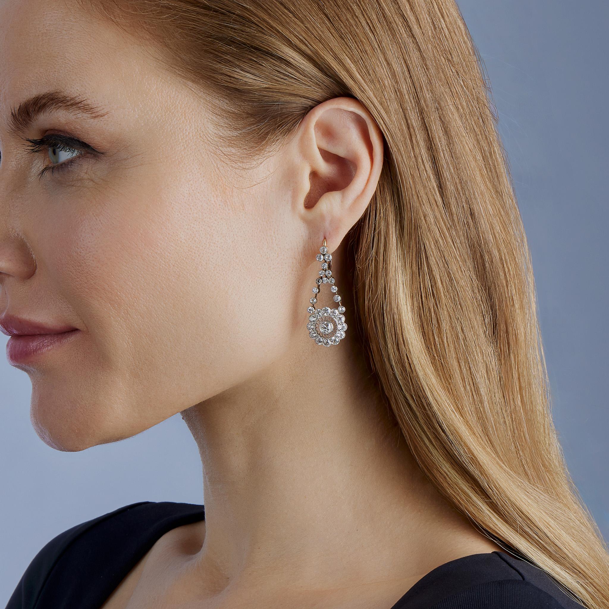 Dating from circa 1890, these diamond pendant earrings are set in platinum-topped 18K gold. Each is designed as a diamond cluster top suspending flexible lines of diamonds joined by knife edge bars and a stylized diamond floret, platinum-topped 18K