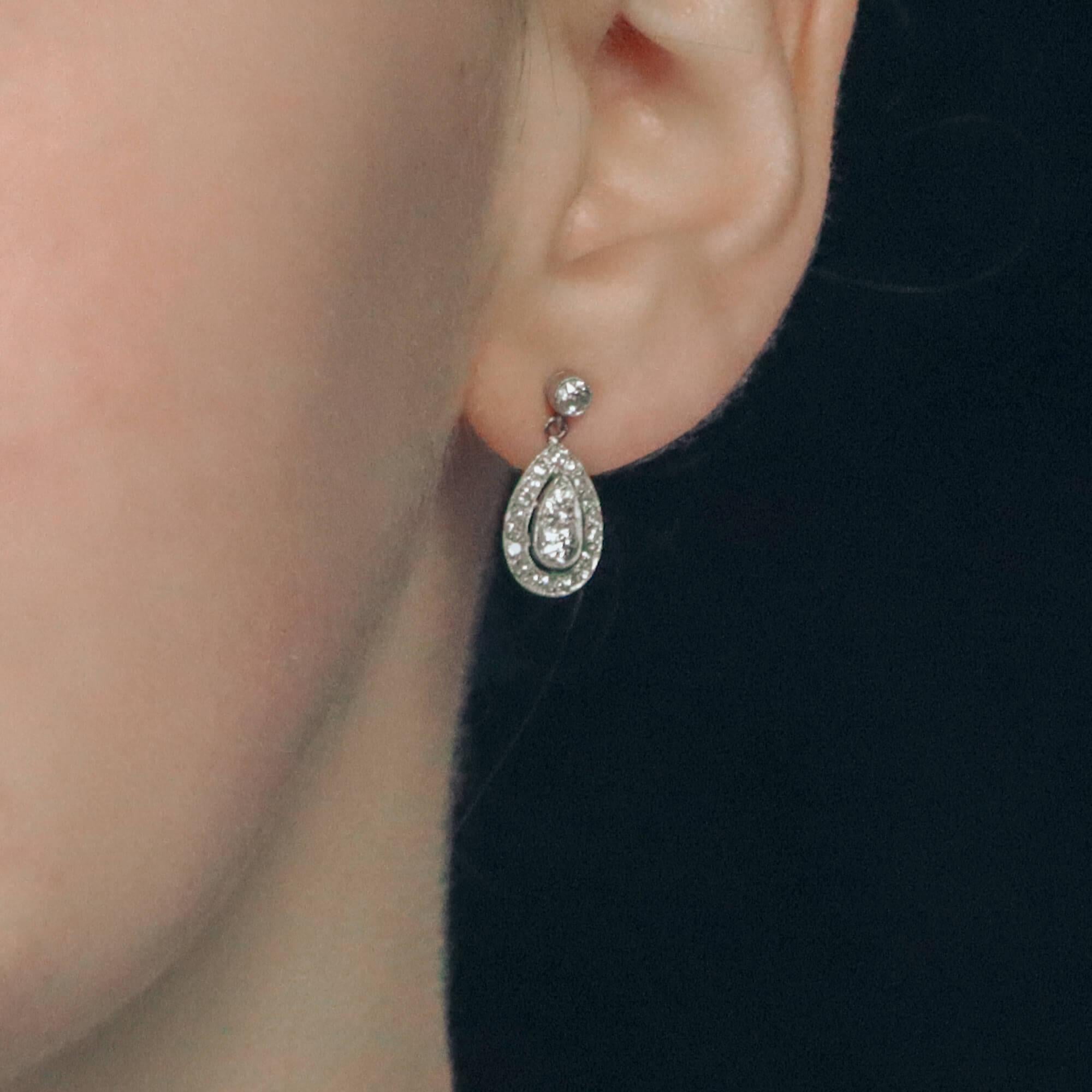 A pair of Edwardian diamond drop earrings in platinum. 
Each earring is designed as a millegrain-set Old European brilliant-cut diamond suspending an articulated pear-shape drop composed of two grain-set Old Mine-cut diamonds amidst a halo of 19