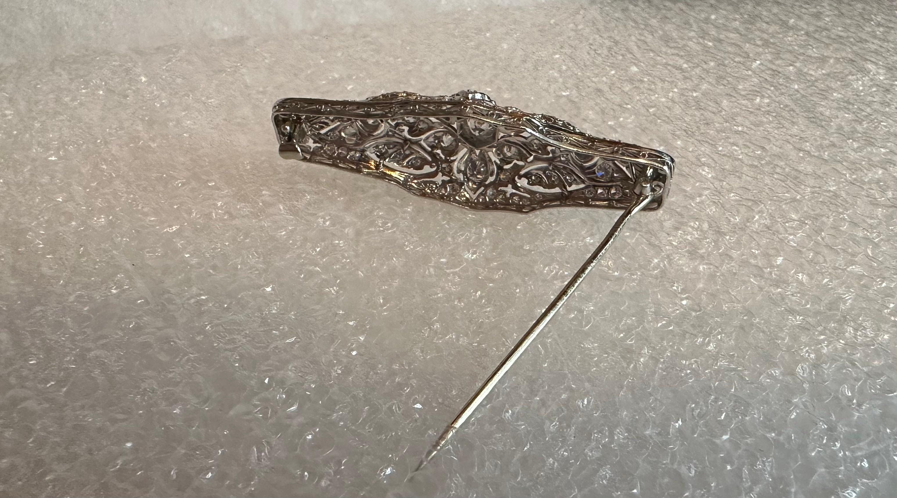 This vintage stunning Edwardian period (1902-1918) diamond & platinum brooch is designed with a stylish pierce work setting beautifully embellished with various size diamonds that showcase a sparkling clean cut center .65 carat diamond. This center