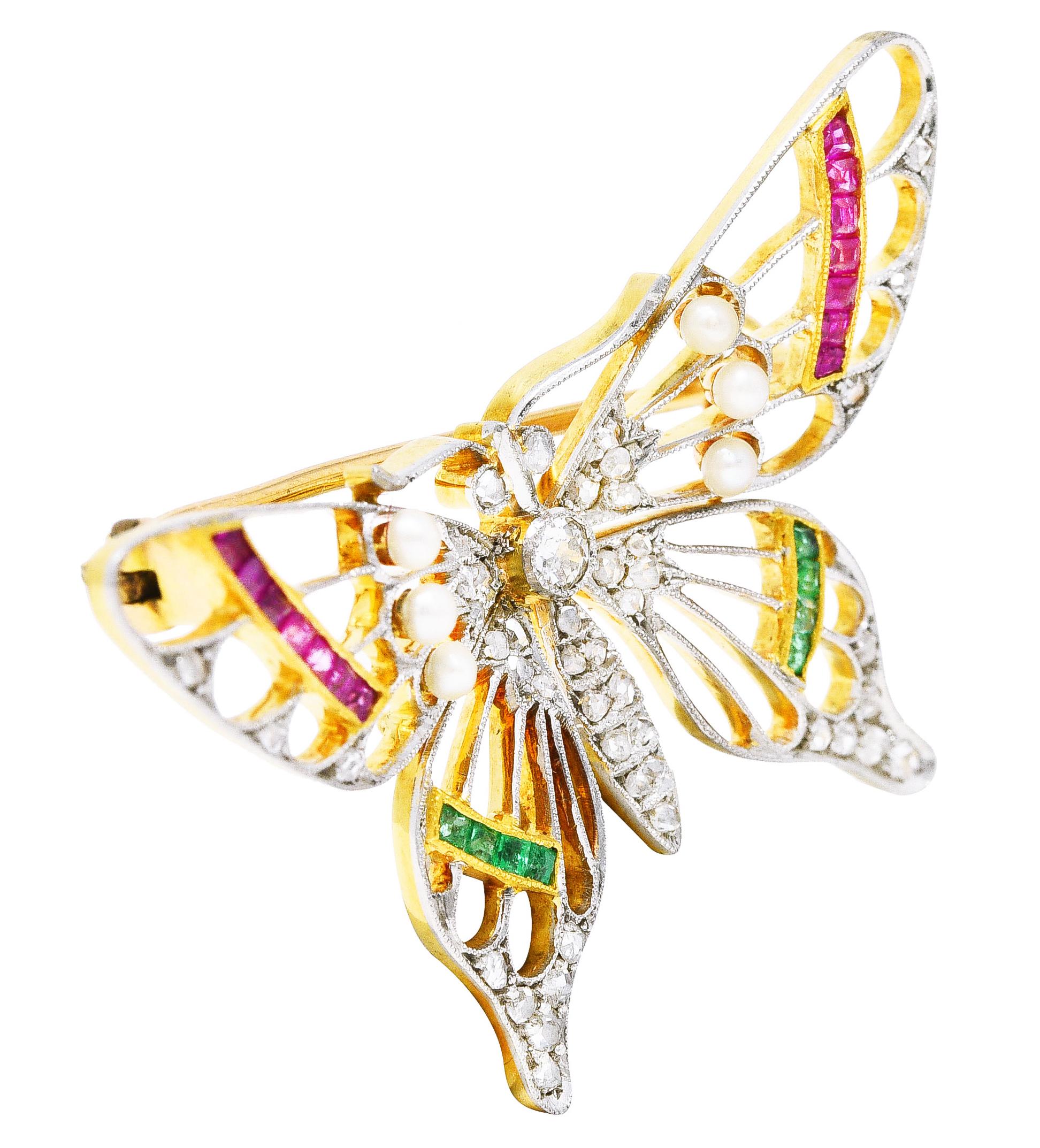 Butterfly brooch is pierced with knife edge veining throughout spread wings. With calibré cut emeralds and rubies channel set in yellow gold. Brightly colored and weighing collectively approximately 0.65 carat. Accented by 2.0 mm round pearls -