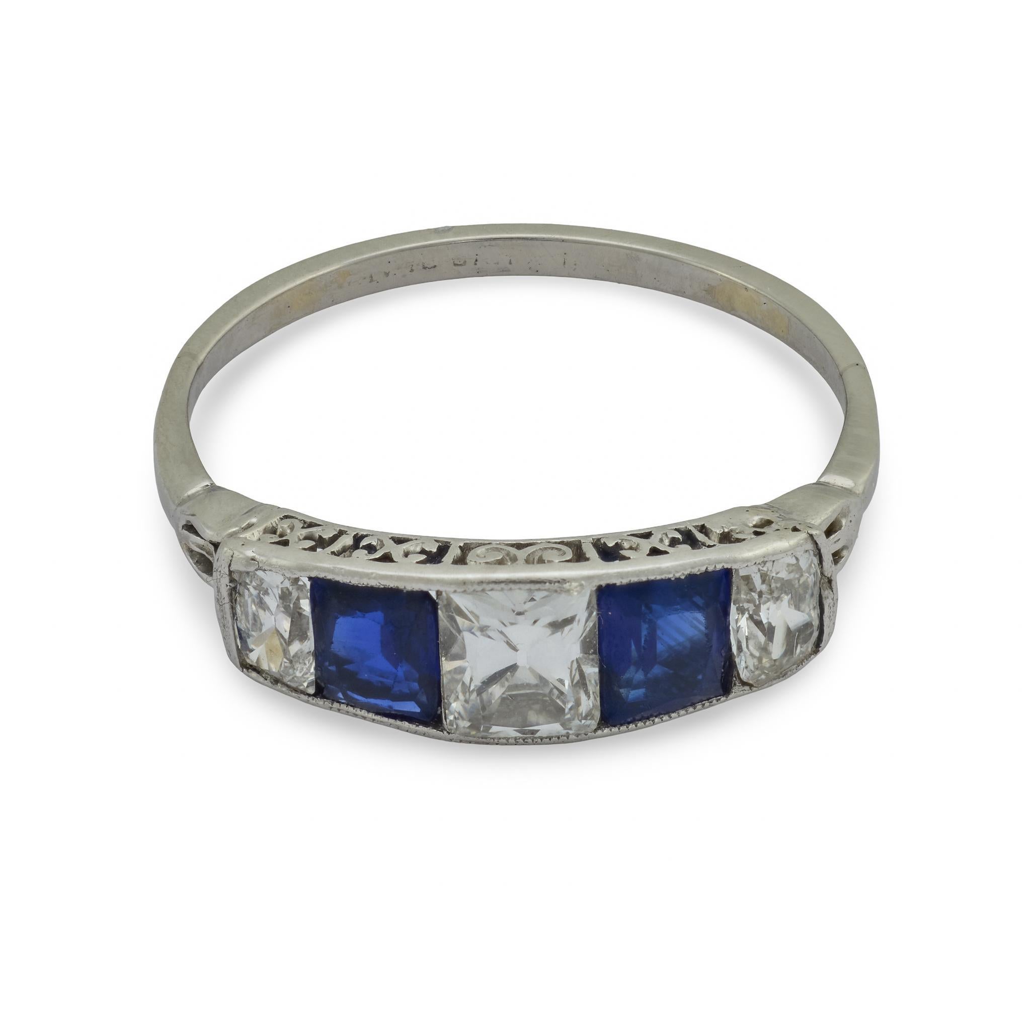 A graceful expression of Edwardian refinement, this five-stone ring showcases a harmonious balance of brilliance and color. Three French cut diamonds shimmer with crisp light, framed on each side by richly hued blue sapphires cut with precise