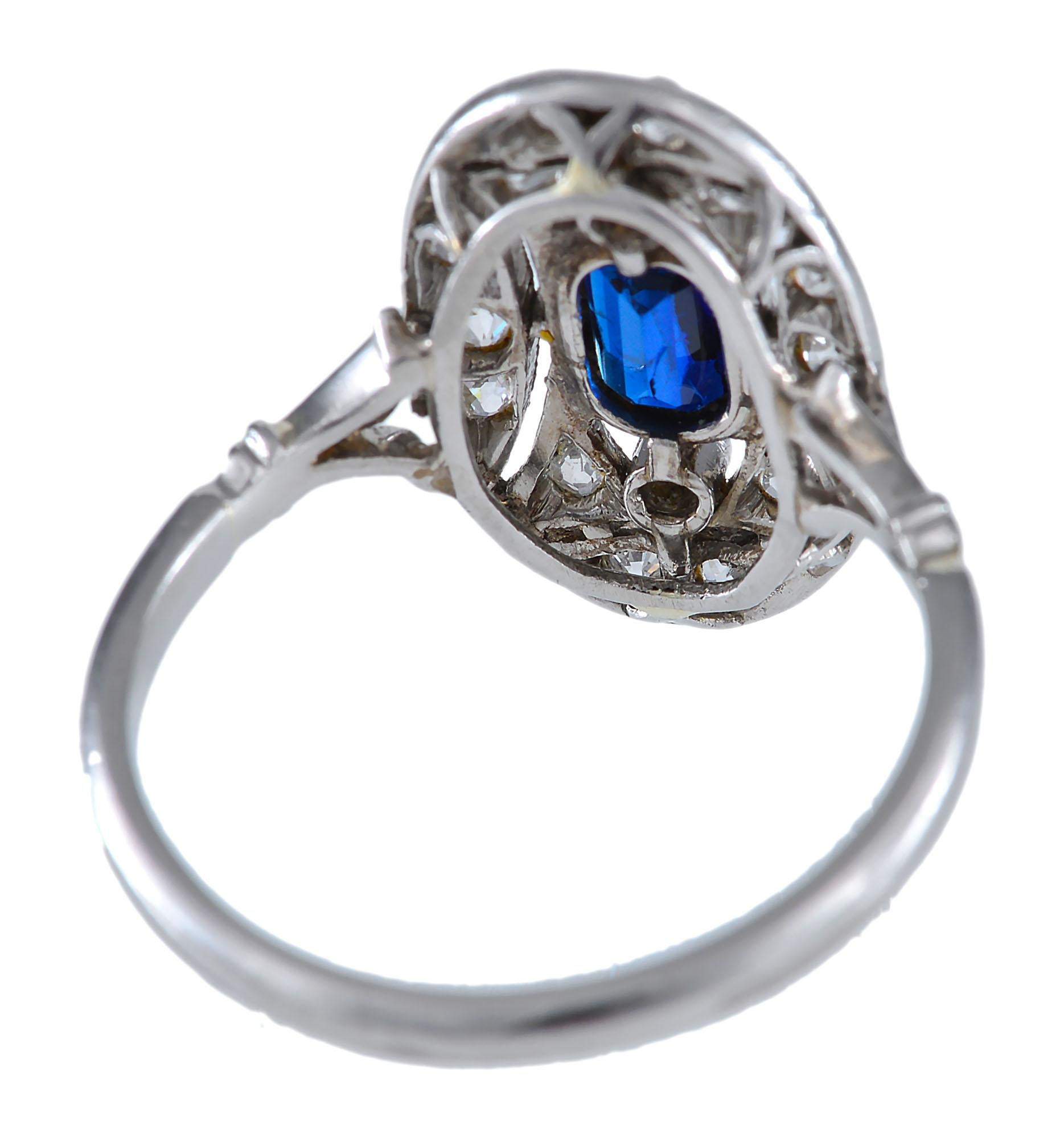 An Edwardian Diamond sapphire ring. The central Sapphire is crowned on either end with a single early Brilliant cut diamond and surrounded with an oval of diamonds within a very fine platinum mount pierced in geometrical shapes. The shoulders of the
