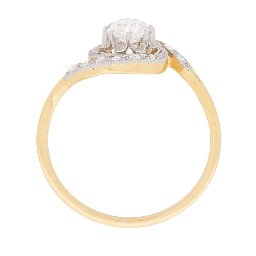 Mirror image swirls of grain-set rose cut diamonds, totalling 0.12 carat, frame a lovely 0.50 carat old cut diamond at the centre of this c.1910s Edwardian era engagement ring. The diamonds are set in platinum over 18 carat yellow gold, with the