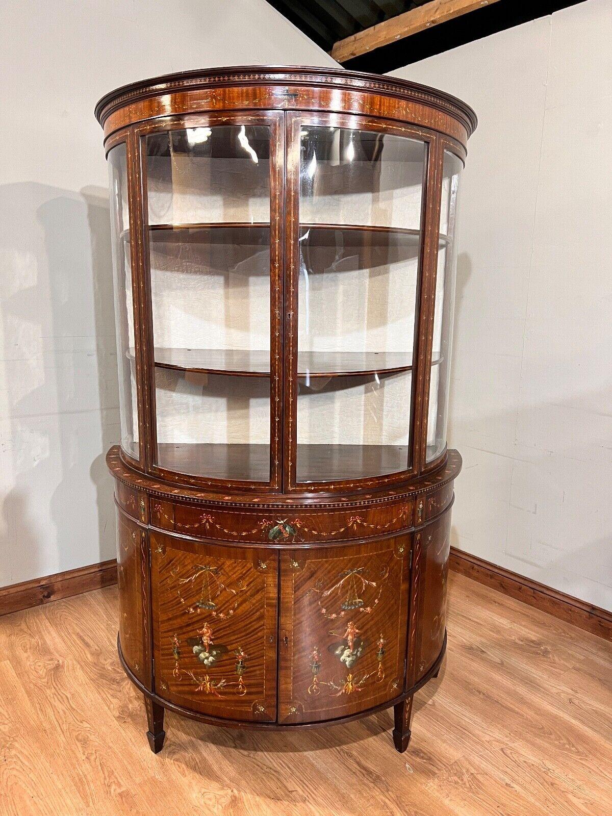 Unusual bow fronted - half round - Edwardian display cabinet
Circa 1900 on this piece which features intricate hand painted designs
Classical designs include urns, cherubs, sashes and garlands all intricately painted
Bottom opens up to reveal large
