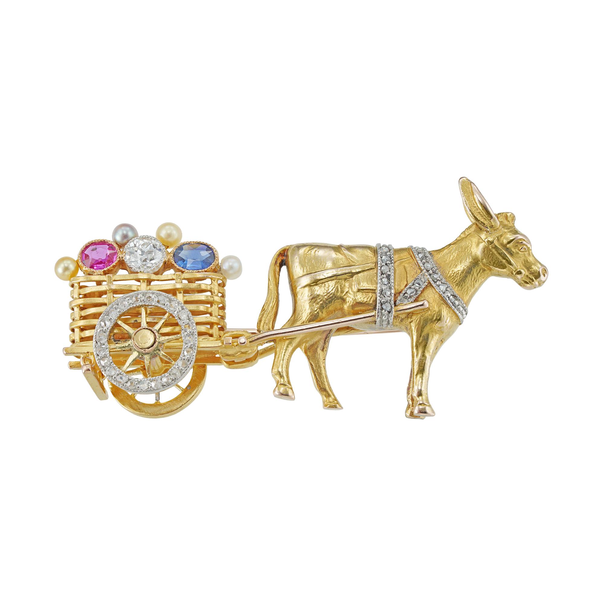 An Edwardian donkey and cart brooch, the yellow gold donkey with diamond-set bridal attached to a cart, the cart designed as a basket with a diamond-set wheel, sitting on top of the cart a ruby, diamond and sapphire with four seed pearls, circa