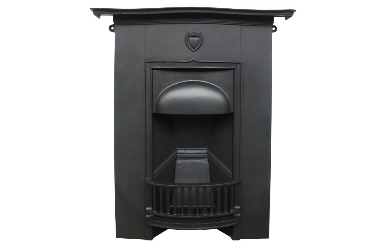 Reclaimed Edwardian early 20th century Arts & Crafts cast iron bedroom fireplace with bow-fronted shelf and frieze. To the centre of the frieze is a high cast shield.

Finished with heat resistant matte black paint this fireplace is complete and