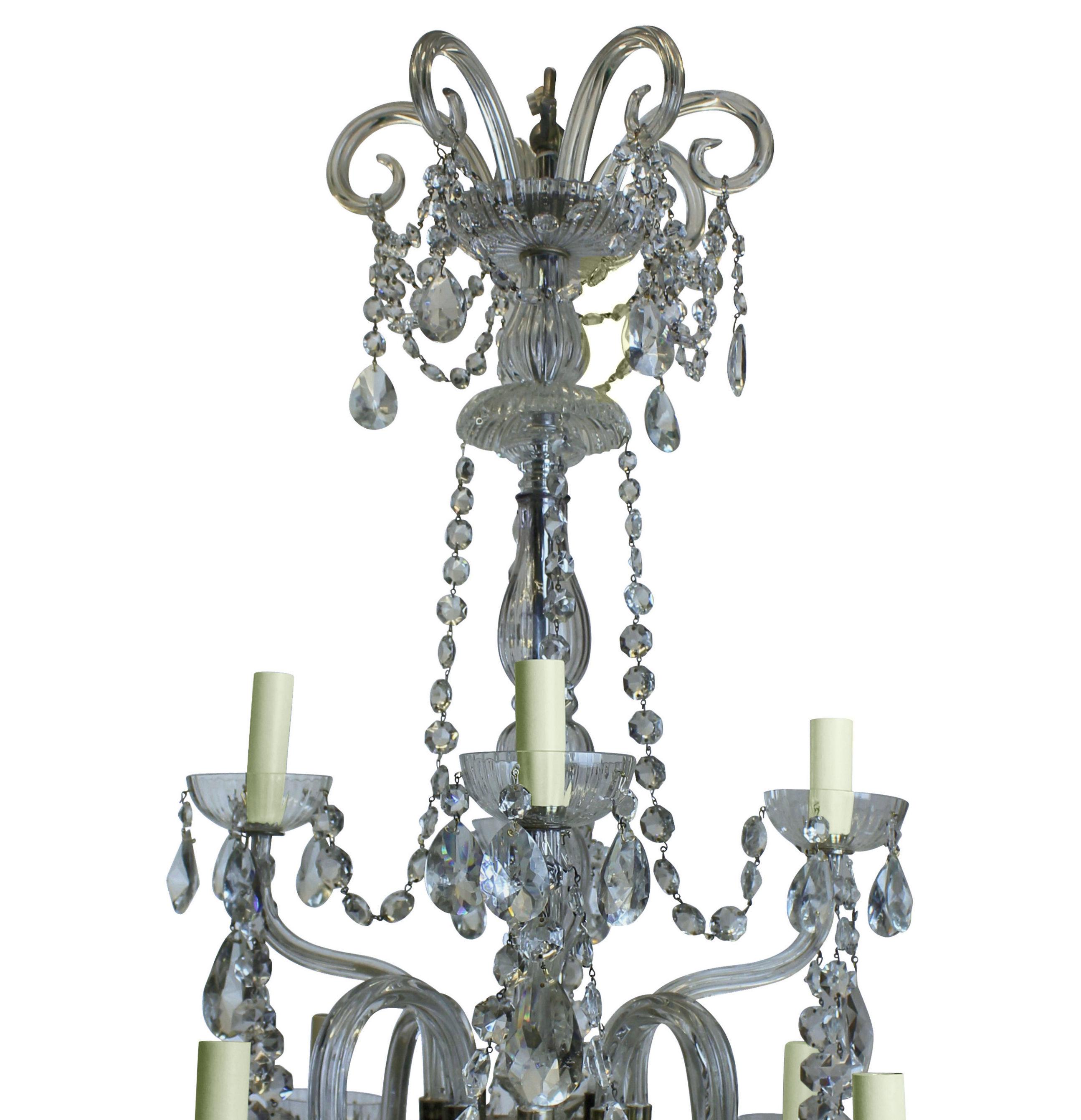 An Edwardian cut glass chandelier, with a tier of four up-swept arms and four down-swept. Hung throughout with cut glass pendants and chains, with a scrolled corona at the top.