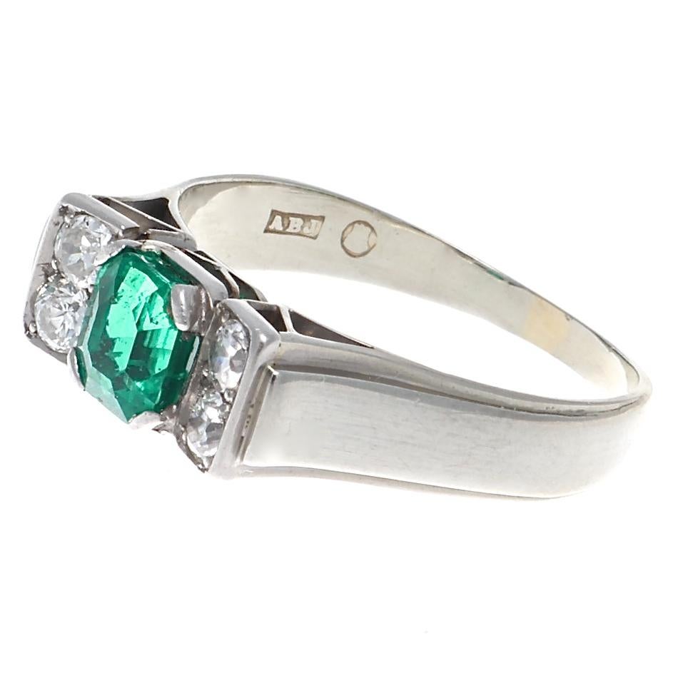 An emerald weighing 0.78 carats sitting in a  prong set ring, framed by four old European cut diamonds G-H in color and SI clarity, weighing approximately 0.40 carats total. Crafted in 18k white gold and stamped with English hallmarks. Size 7 1/4