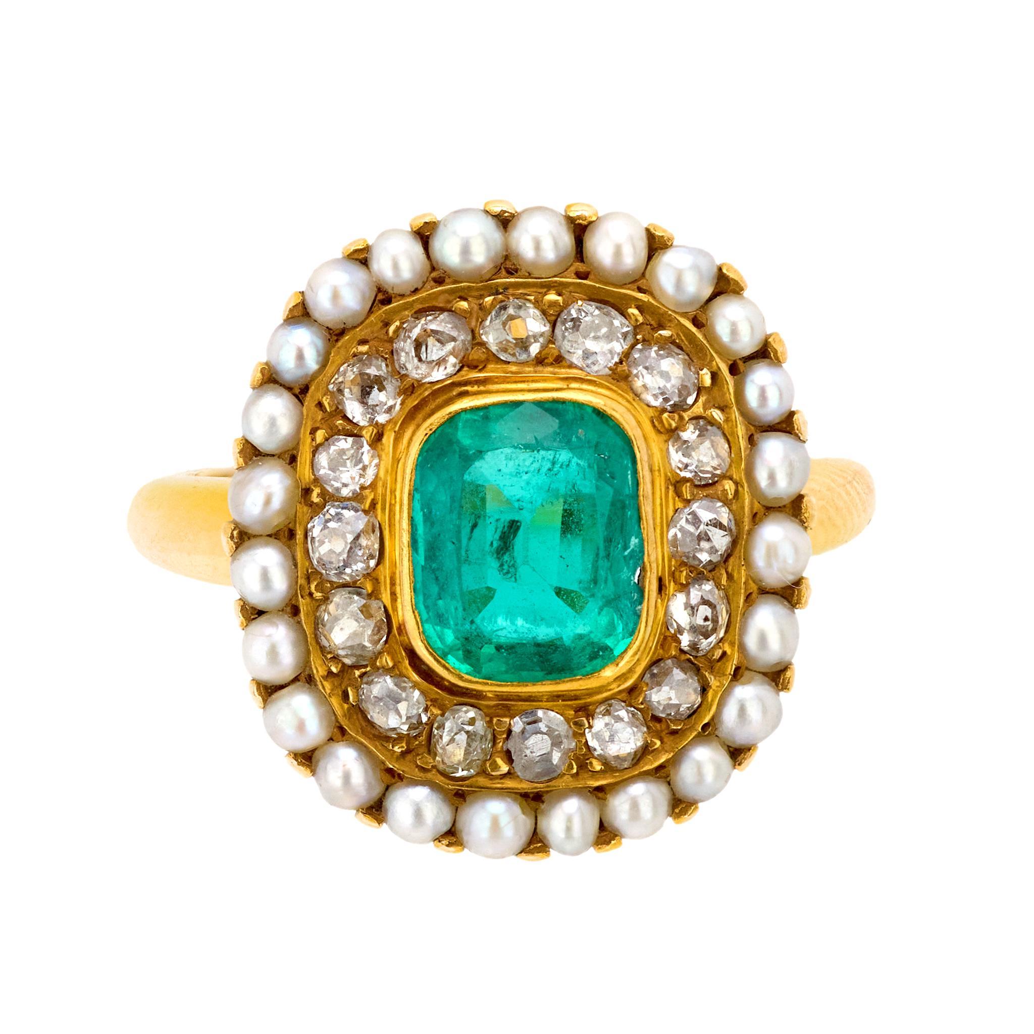This Edwardian 14k yellow gold ring features a cushion cut emerald of approximately 1.10 carats, accented by 16 old mine cut diamonds totaling approximately 1 carat, H color, SI clarity, and delicate seed pearls. A refined and intricate design