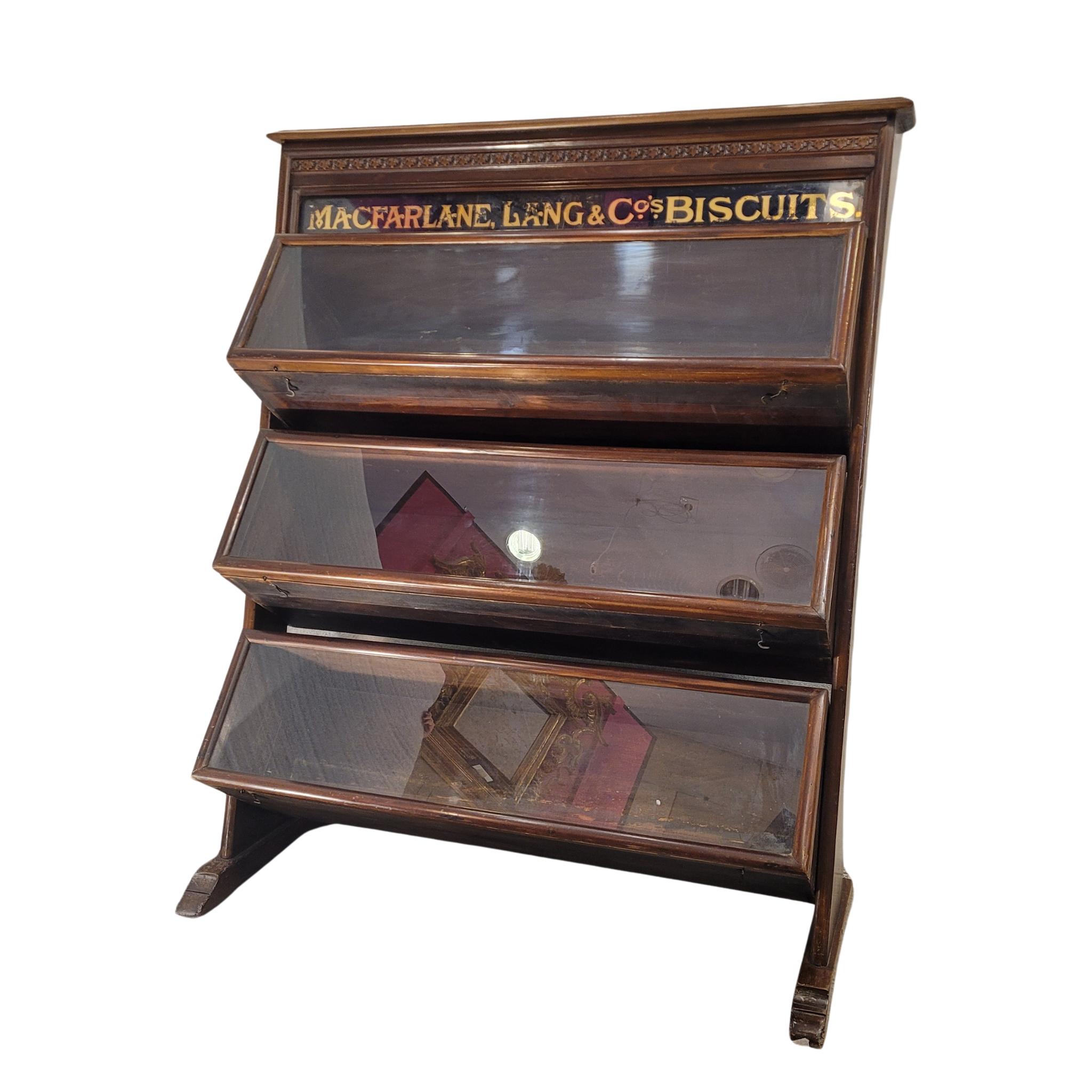 A unique and singular piece of furniture is a biscuit display cabinet from the early 20th century, made of wood and glass. This special shelf was designed to hold cans or packages at an angle, so that they could be easily accessed and, at the same
