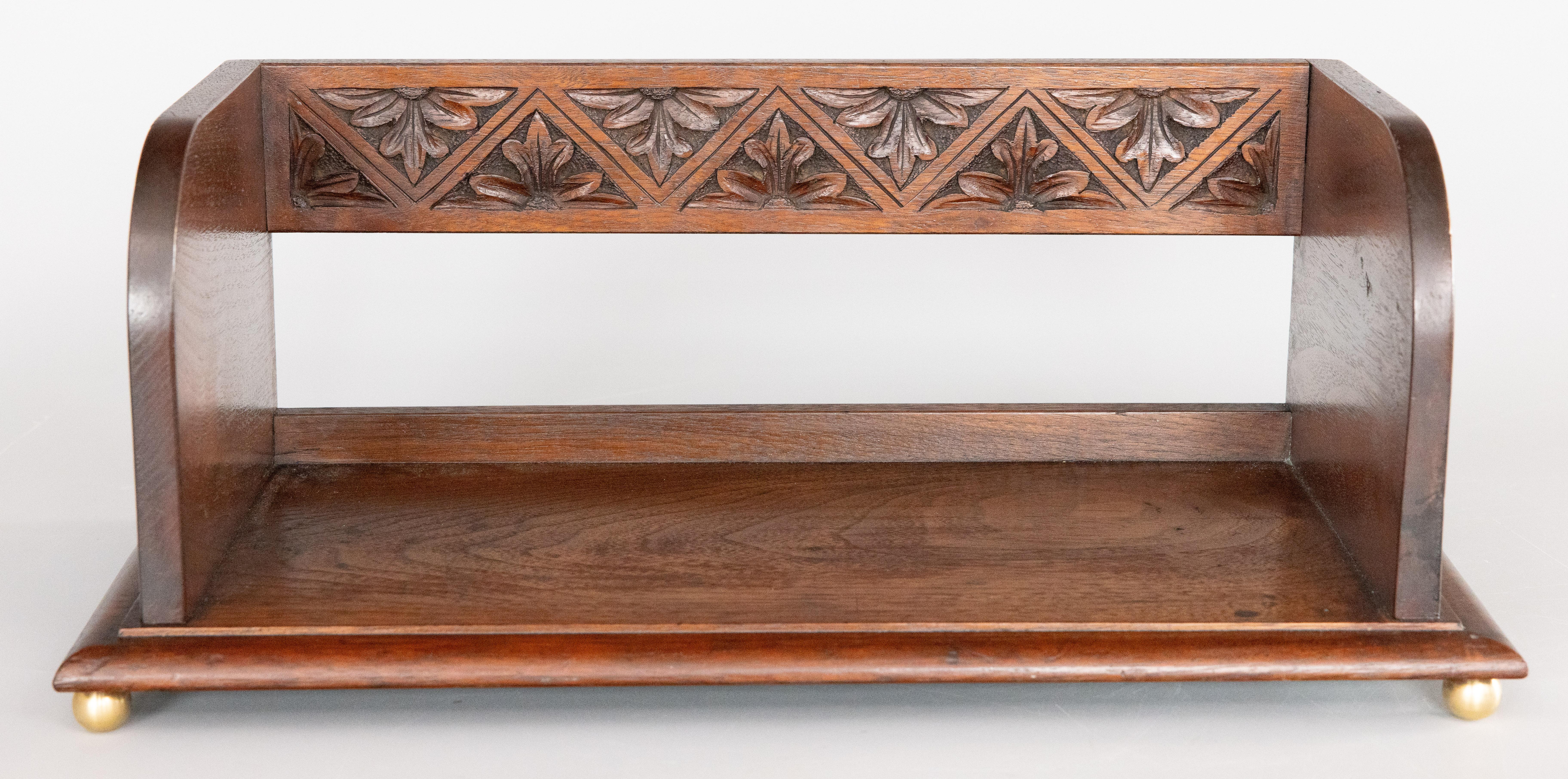 A fine antique early 20th Century English mahogany carved book trough / book rack / book stand. This beautiful table top book stand is well made with hand carved floral designs and brass ball feet. It would make a handsome addition to a desktop or