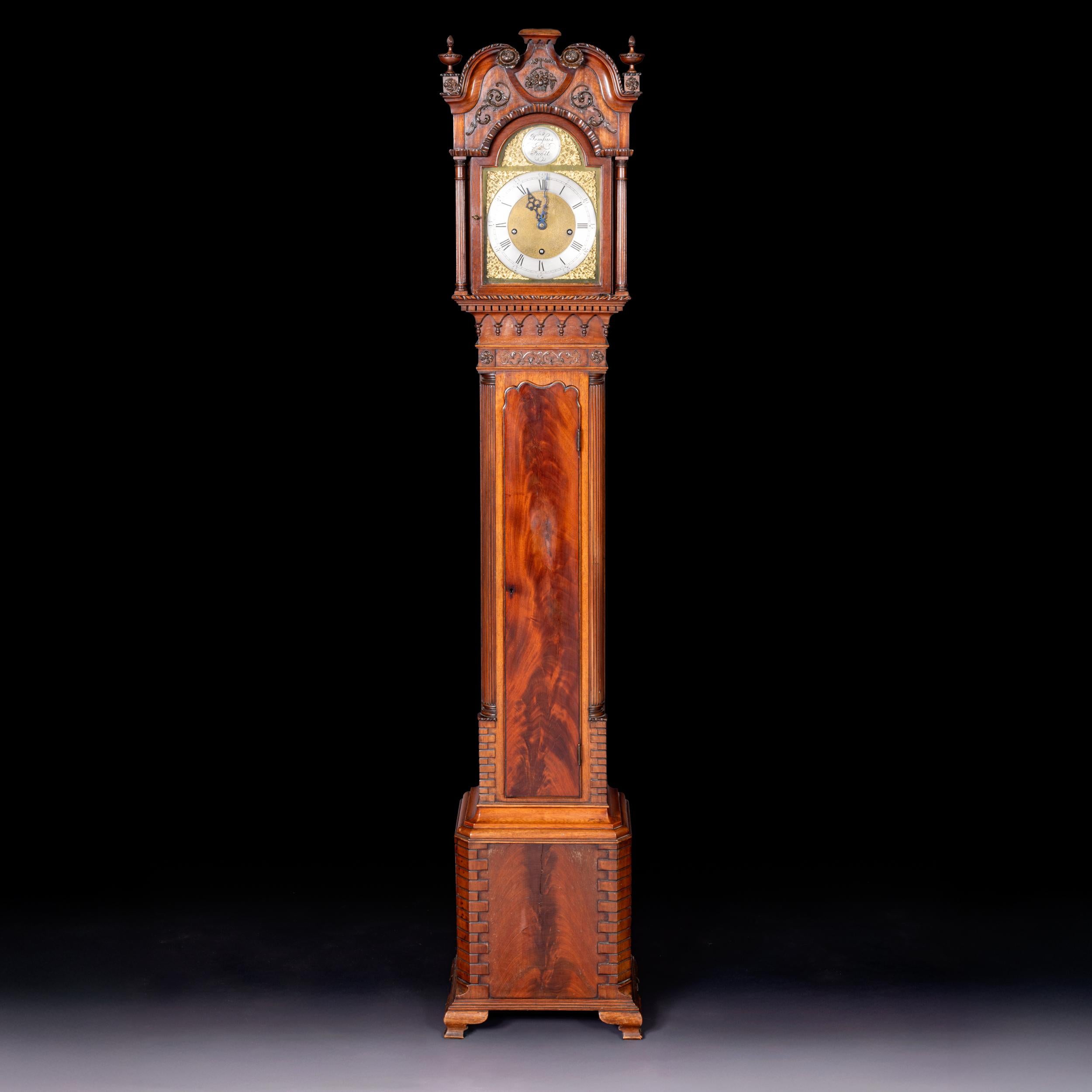 An attractive late 19th century miniature Grandfather longcase clock sometimes referred to as a Grandmother clock.  The arched hood surmounted by a broken swan-neck pediment with carved roundels and urn finials, centred by a floral and scroll-carved