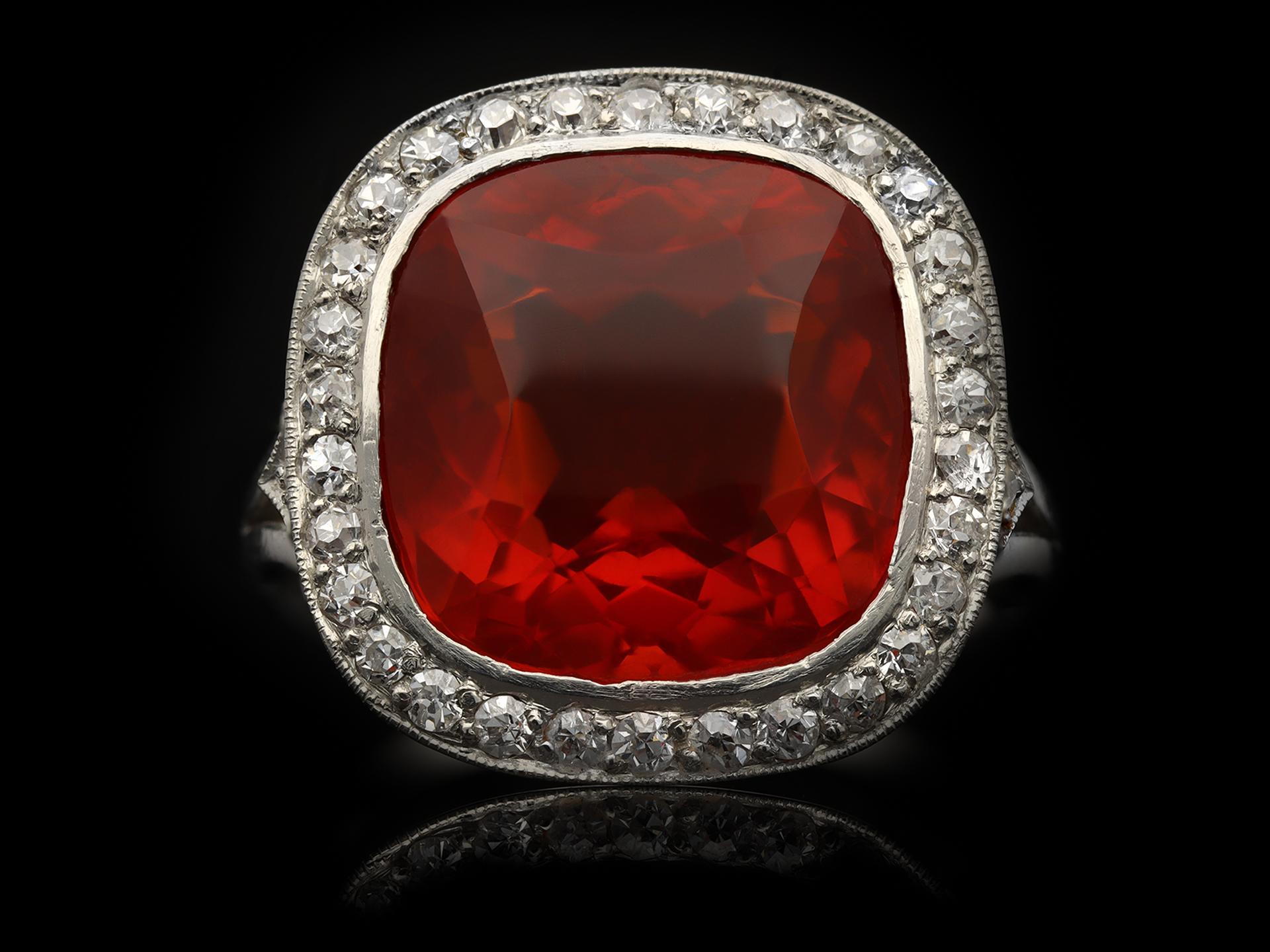 Edwardian fire opal and diamond coronet cluster ring. Set to centre with a cushion shape old cut natural unenhanced fire opal in an open back rubover setting with an approximate weight of 6.75 carats, further set with thirty six round old cut
