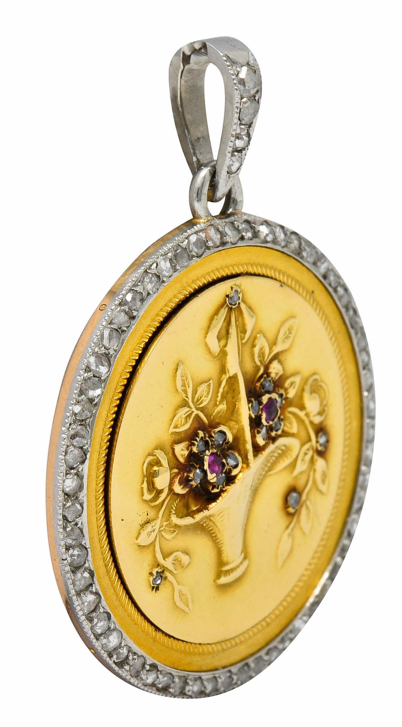 Large circular locket depicts a flourishing basket of florals with ruby and rose cut diamond accents

With a deeply ribbed surround and a platinum halo accented by rose cut diamonds

Weighing in total approximately 0.82 carat with quality consistent