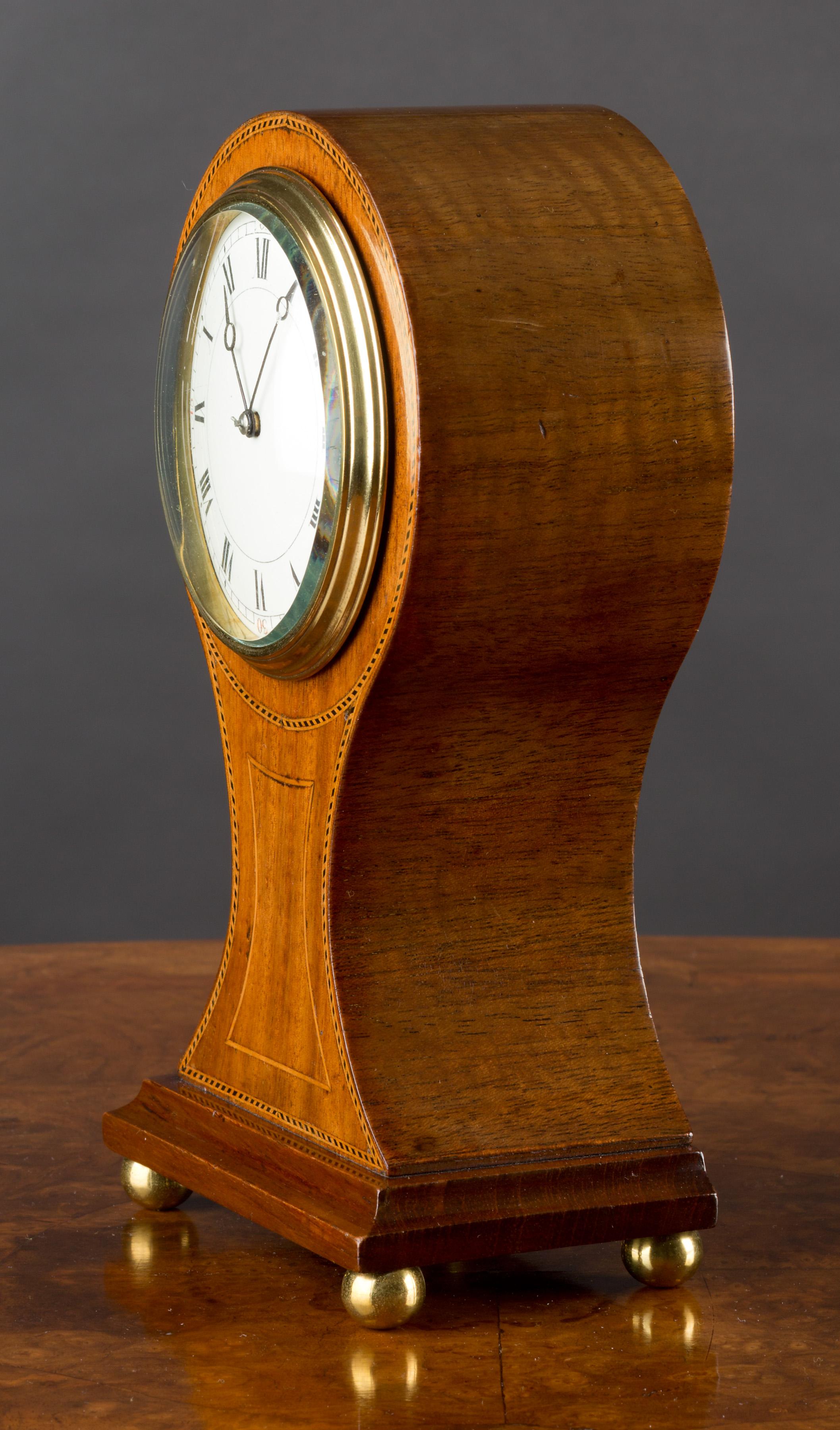 Edwardian mahogany Balloon clock standing on brass ball feet with boxwood and ebony chequered stringing and satinwood line inlay. 

Enamel dial with Roman numerals and original ‘moonpoise’ hands.

 Eight day French movement with platform