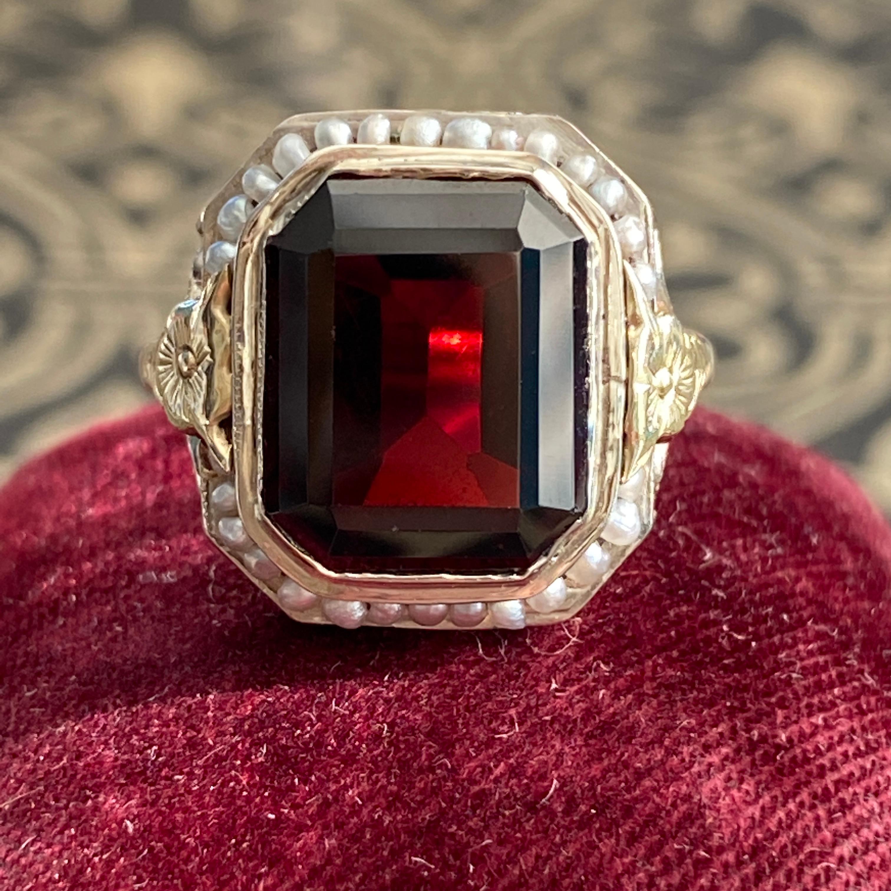 Details: 
A beautiful deep red garnet ring from the Edwardian Era (ca 1900's) era. This lovely two tone ring is crafted in 14K white gold with yellow gold details. The filigree on the sides of the setting is sweetly decorated with with pansy flowers