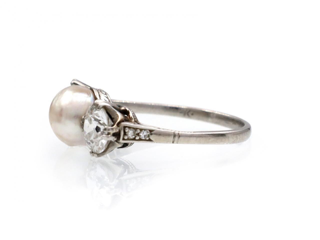 Edwardian natural pearl and diamond three stone ring in platinum. Centred with a natural saltwater pearl flanked to either side with two round Old European cut diamonds in split claw settings, to a three stone design with curving claws, engraved